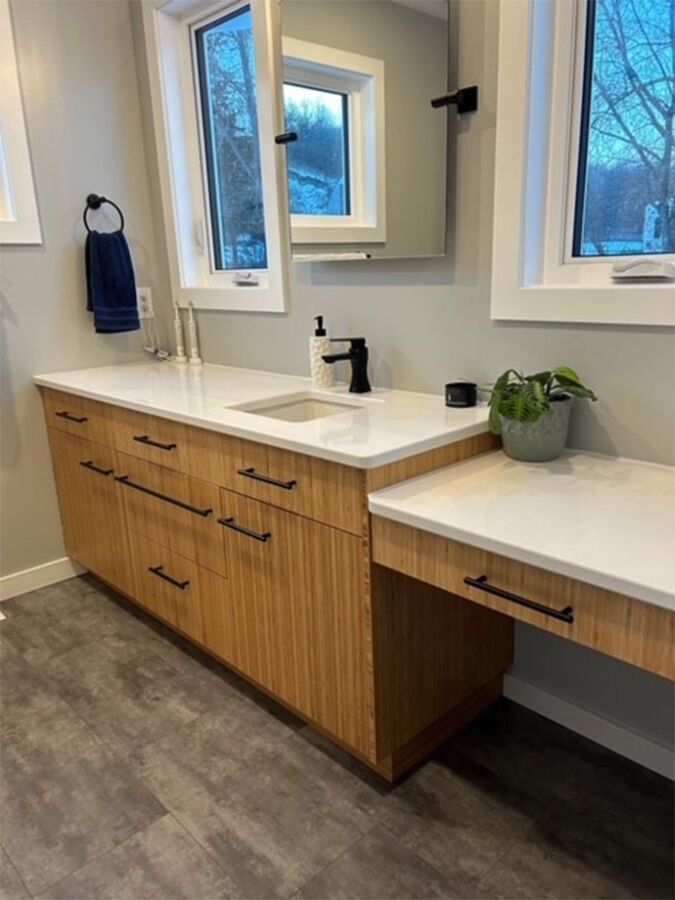 Bathroom vanity with a wooden cabinet, white countertop, built-in sink, black faucet, and a small potted plant.