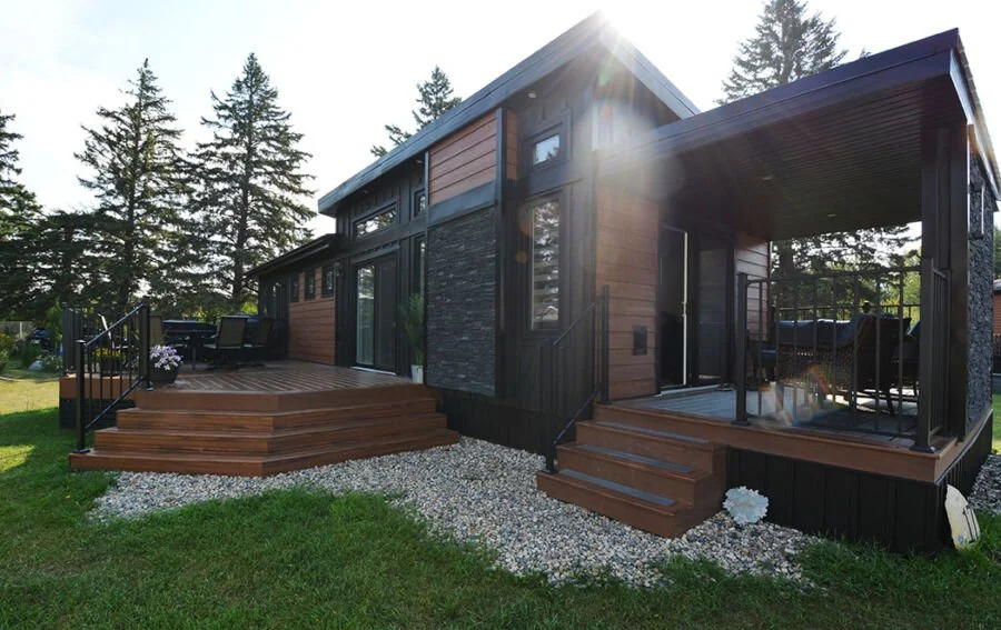 Modern two-story house with large wooden decks, black trim, and surrounded by tall pine trees.
