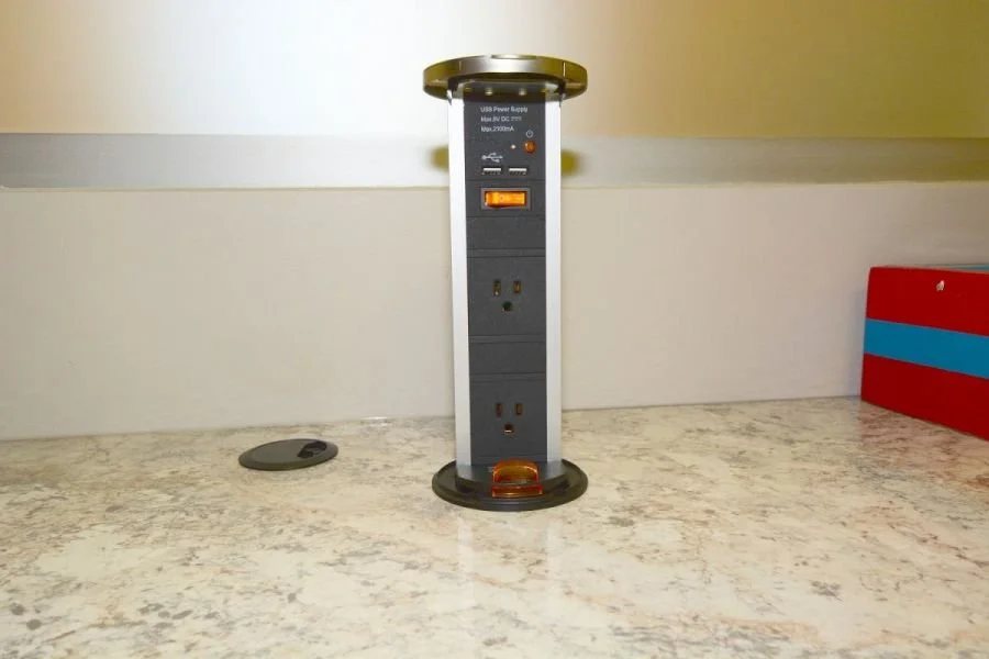 Vertical power strip with multiple outlets and switches on a countertop, with a small round object nearby.
