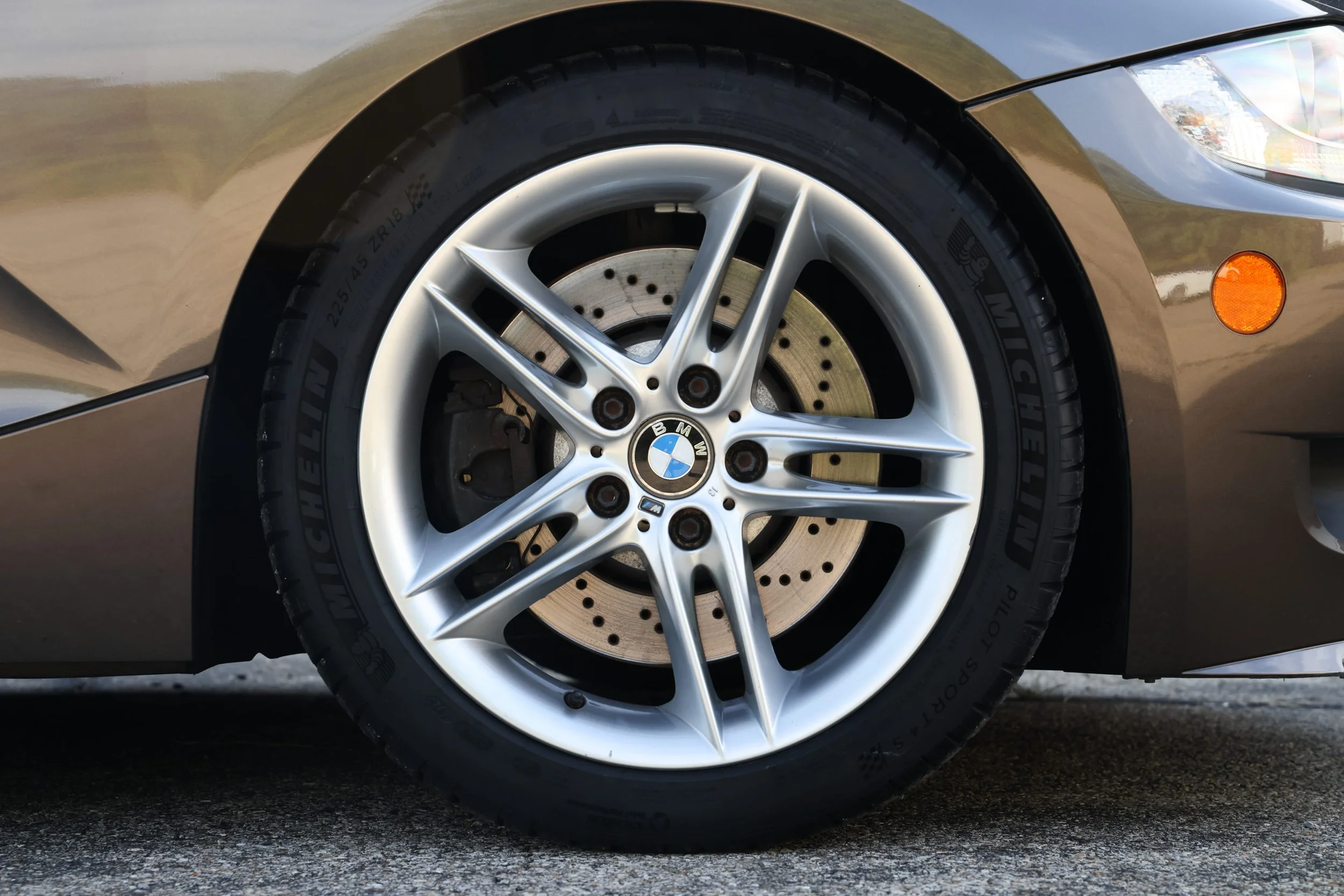 Close-up of a BMW car wheel with a silver alloy rim, black tire, and visible brake disc, parked on a rough pavement.