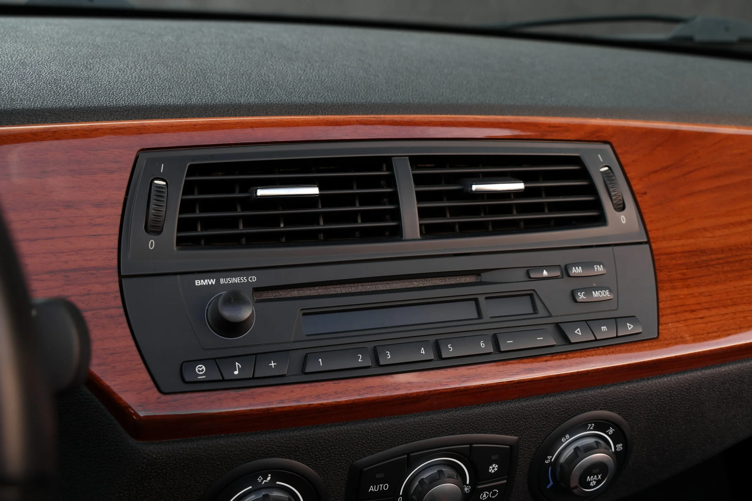 Dashboard of a vehicle with air vents and control buttons, featuring a wooden trim and various climate control knobs.