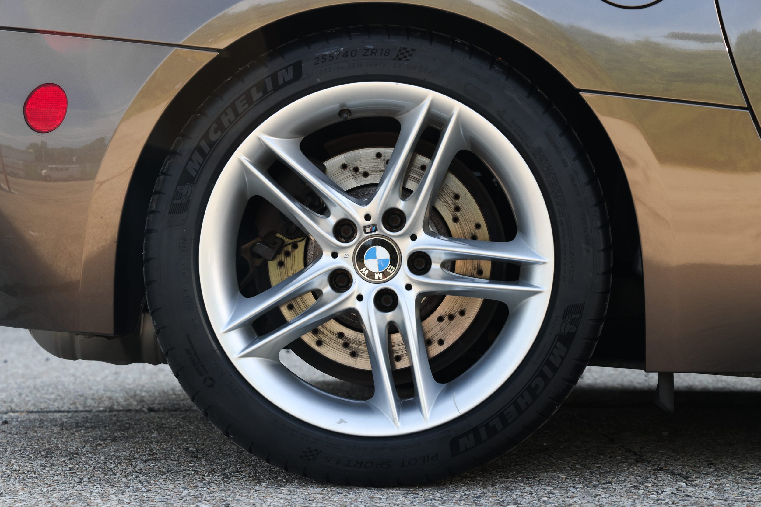 Close-up of a car's wheel featuring a BMW logo, five silver spokes, a tire with the Michelin brand, and a view of the brake disc behind the wheel.
