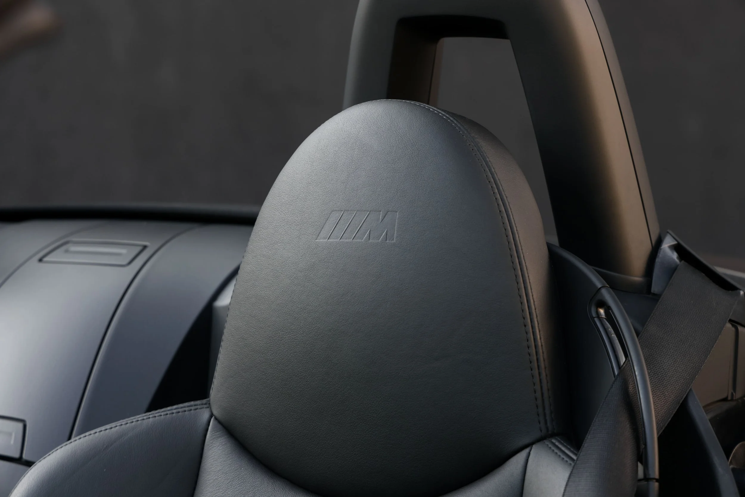 Close-up of a car seat headrest with the BMW M logo embossed on it, made of grey leather, in a modern vehicle interior.