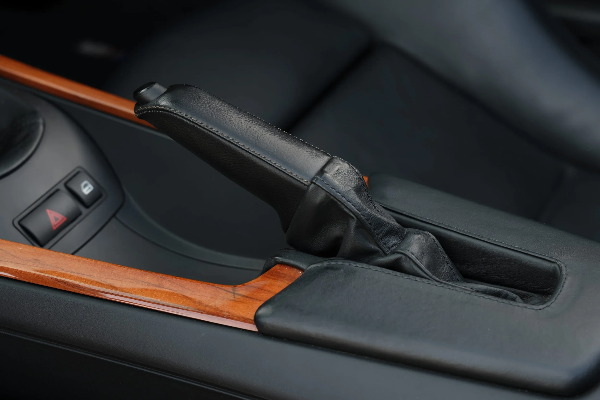 Close-up of a black leather handbrake lever in a car interior, with a wood trim surrounding it and a part of the dashboard visible.