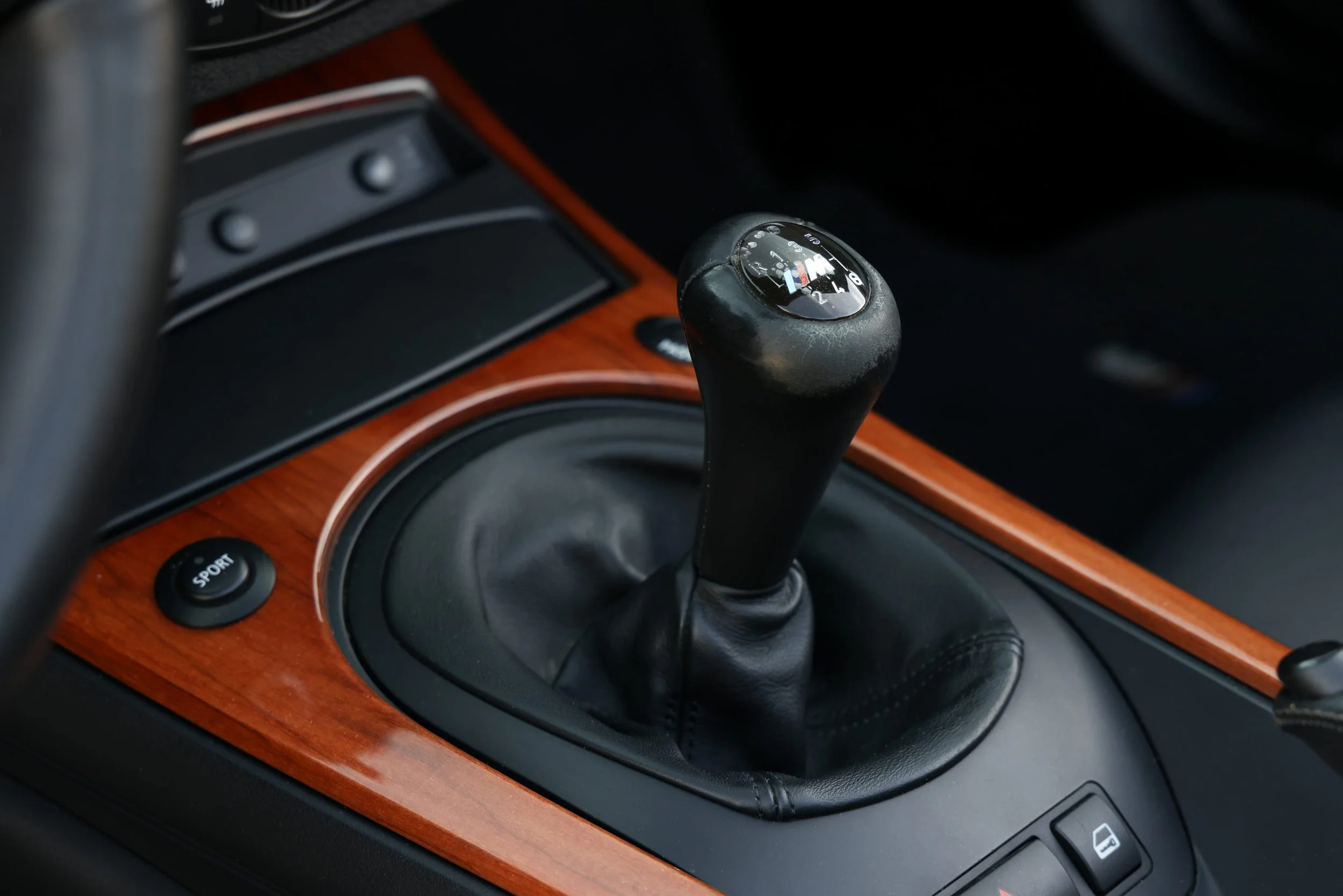 Close-up of a manual gear shifter in a car with a black top and a logo, on a vehicle's wooden and black interior.