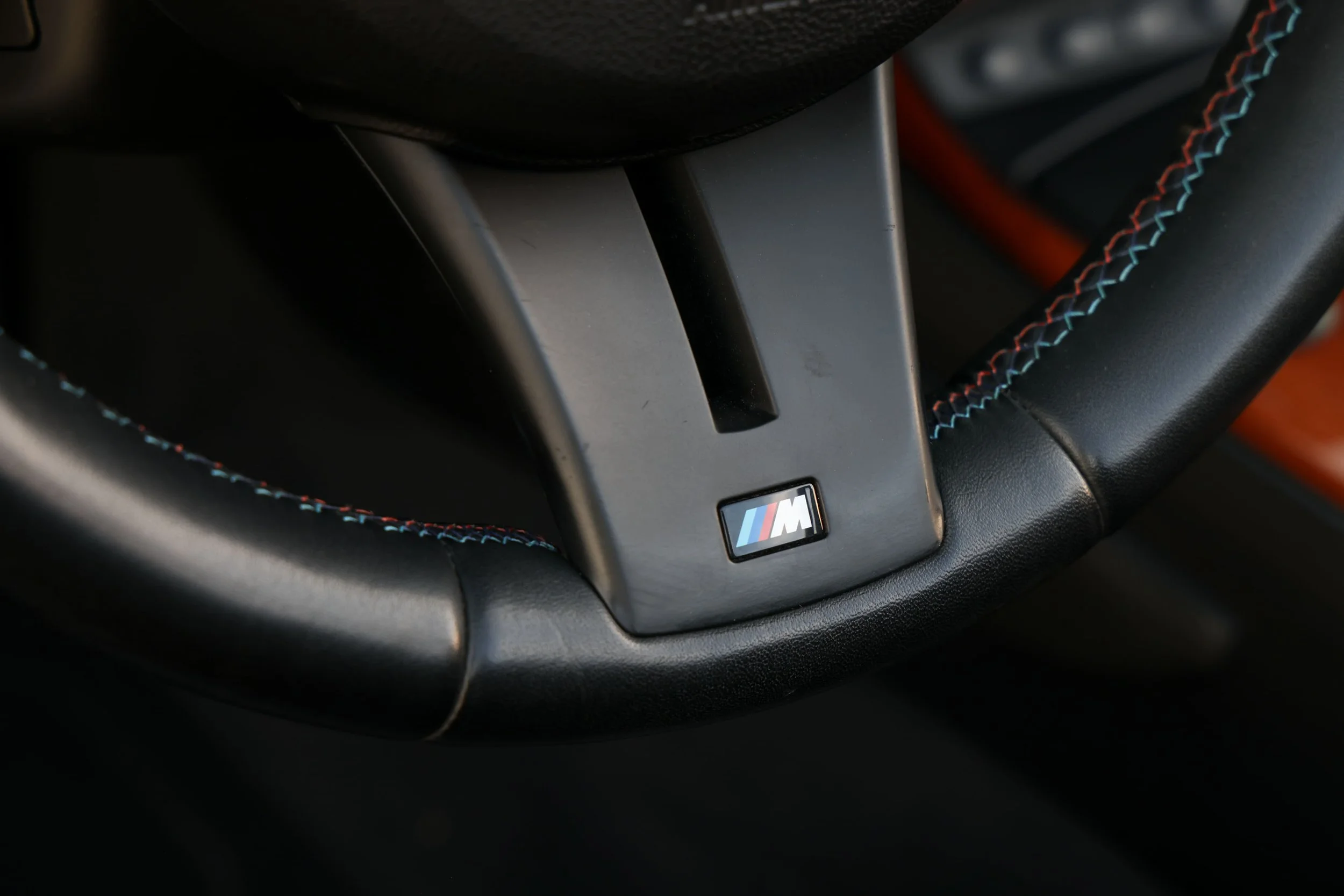 Close-up of the interior of a BMW M car, showing part of the steering wheel and dashboard with a BMW M badge.