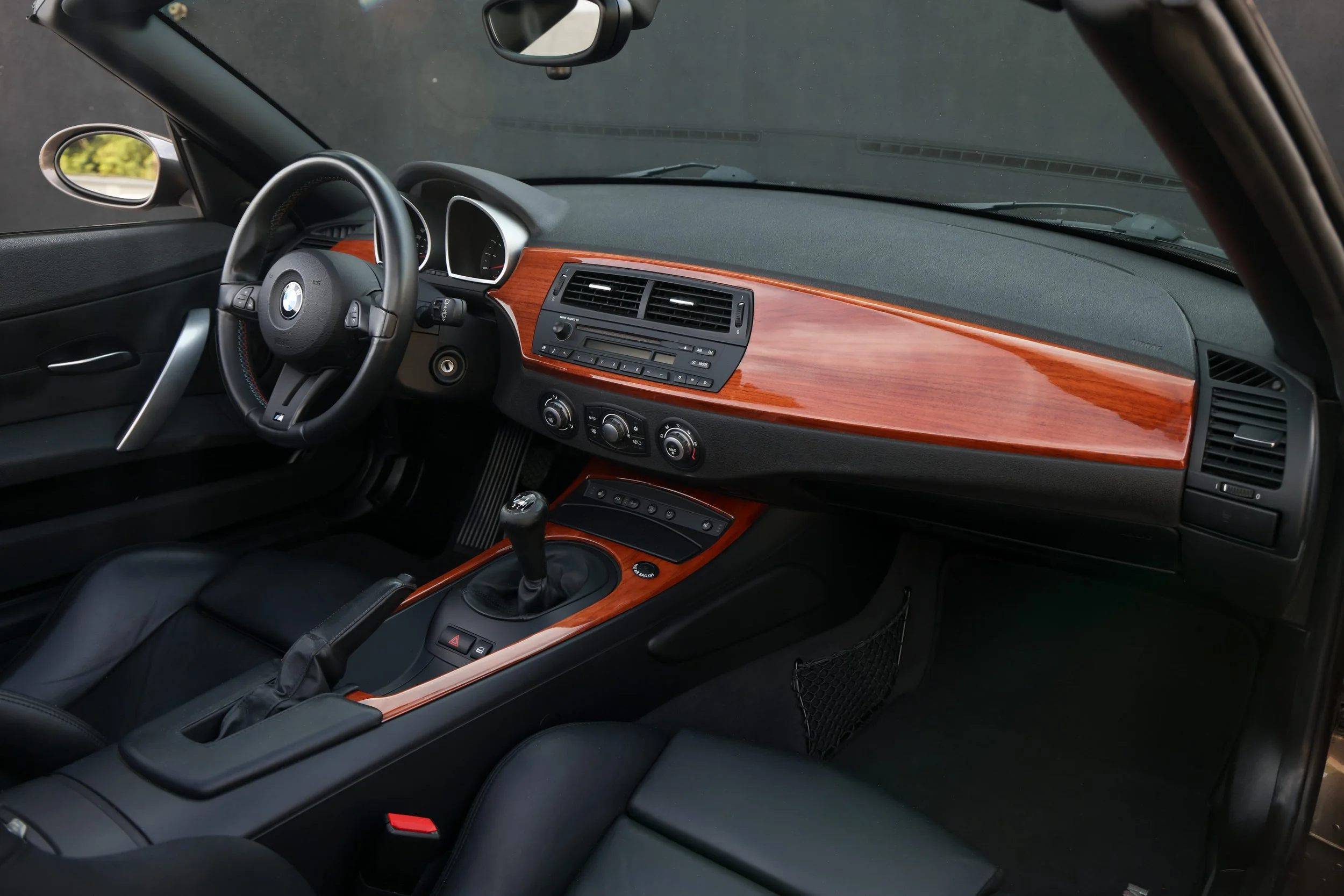 Interior of a car showing the dashboard, steering wheel with BMW logo, and a gear shift, with a wooden panel and various controls.