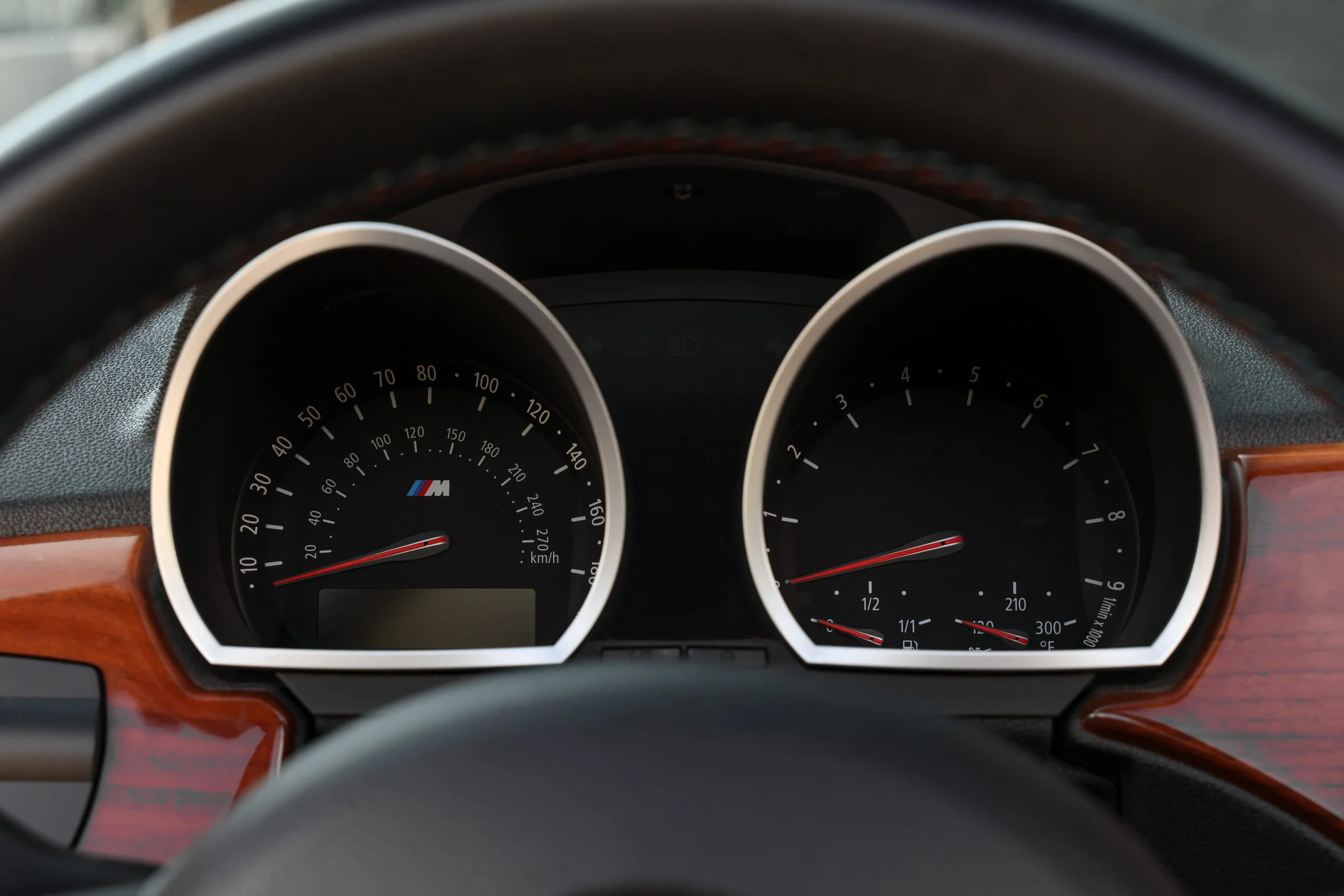 Close-up of a car's dashboard gauges with the speedometer, tachometer, and fuel gauge visible, featuring BMW M logo at the center.