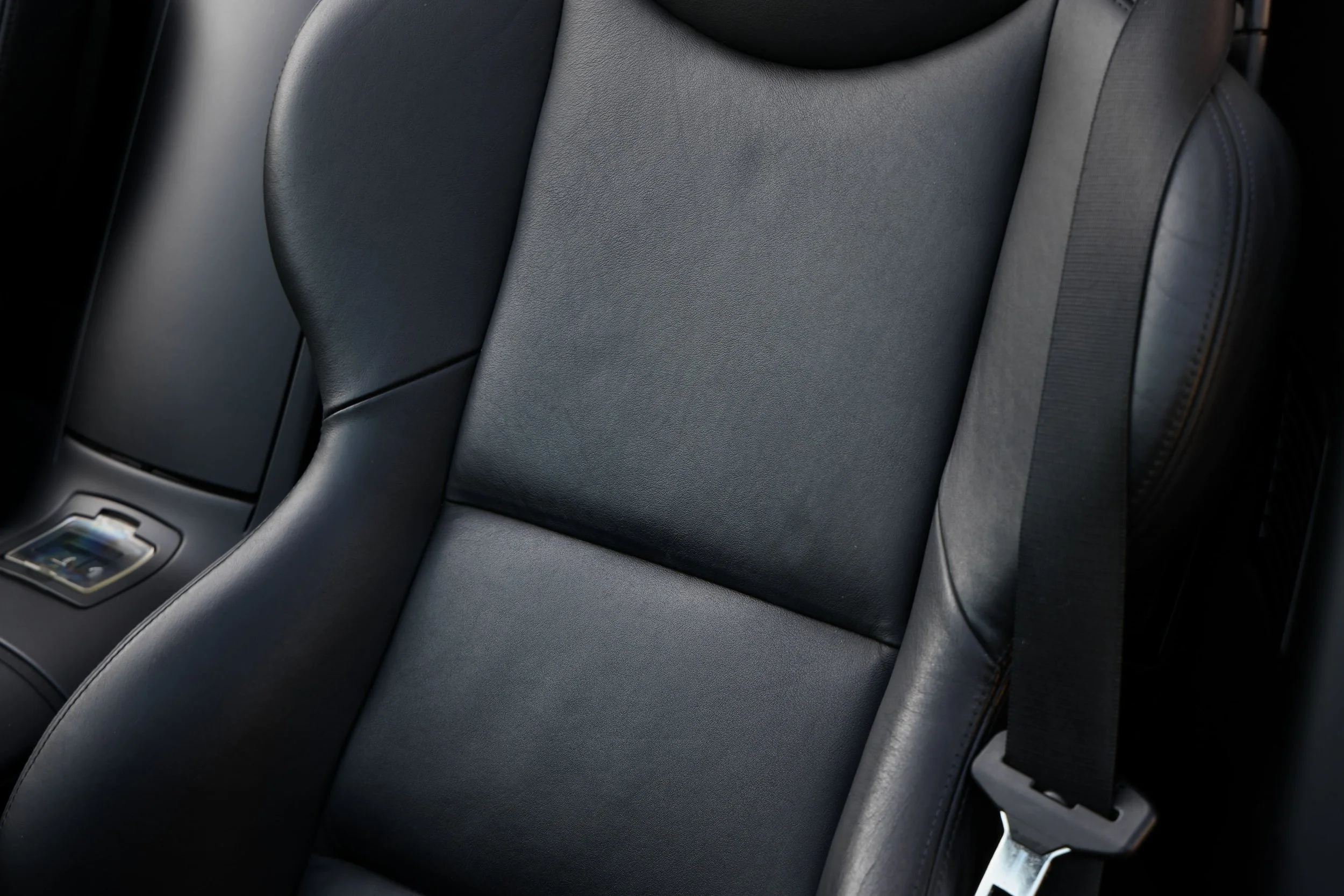 Close-up of a black leather car seat with visible stitching and a sleek, smooth surface.