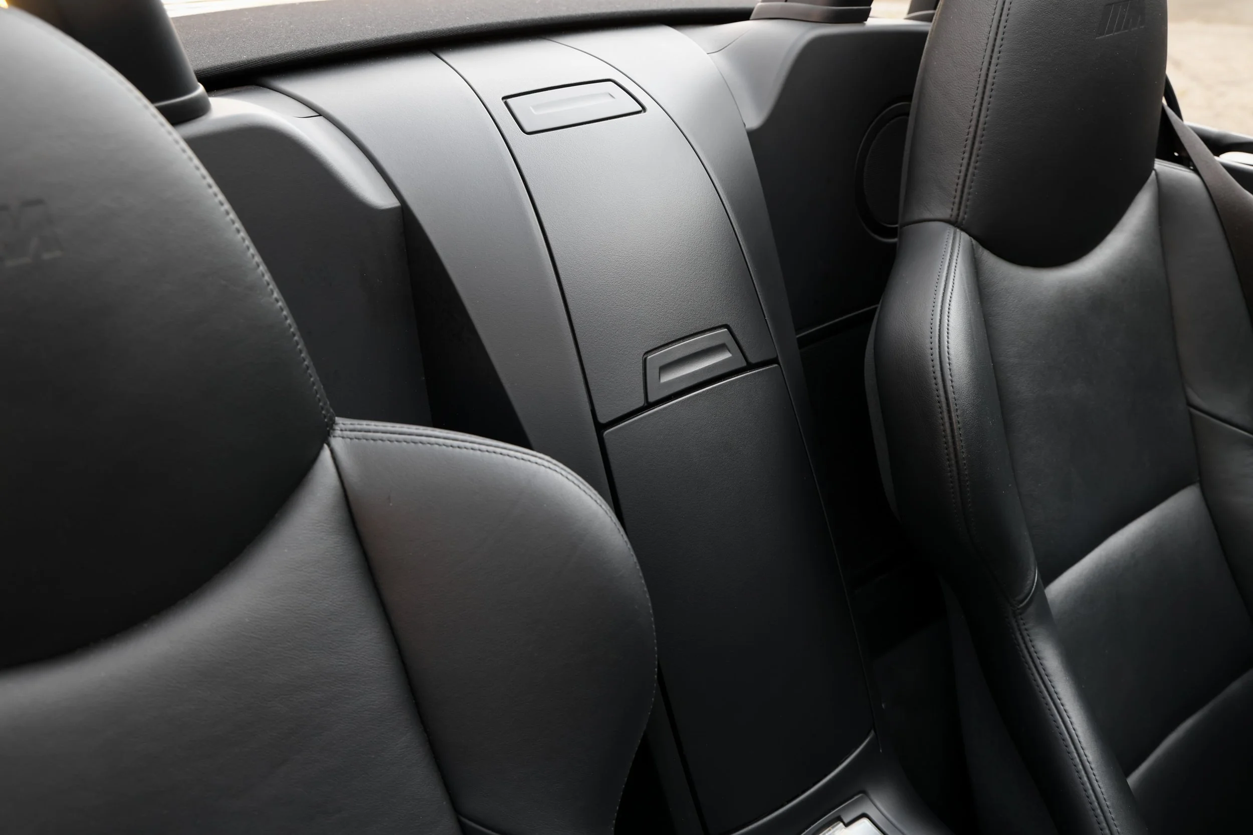 The interior of a vehicle, showing the back of front seats with black leather upholstery and a center console with storage compartments.