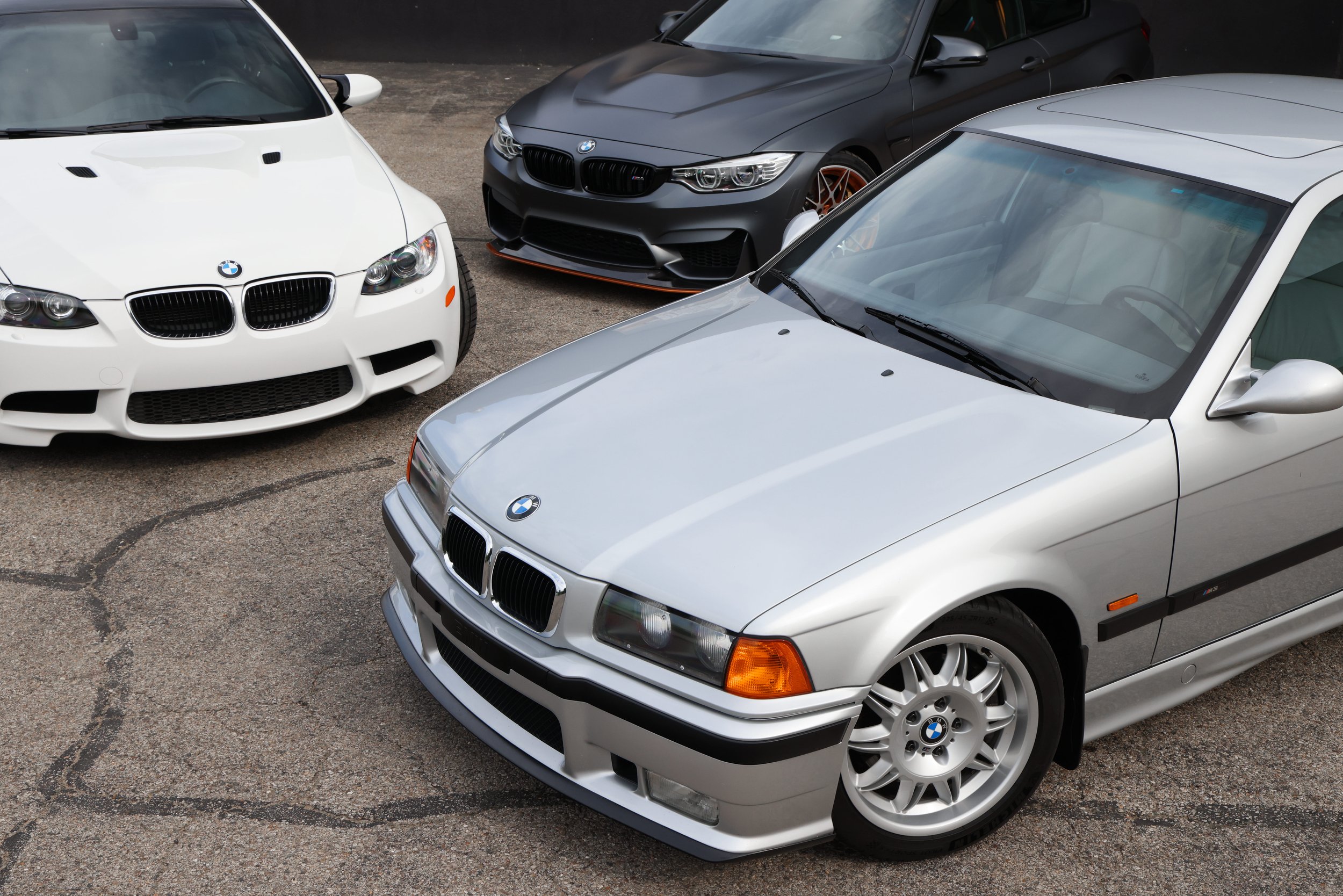 A collection of vintage BMW cars, including a white car with a checked decal on the hood and a red car with dual round headlights, parked inside a modern showroom with wooden floor and decorative ceiling lights.