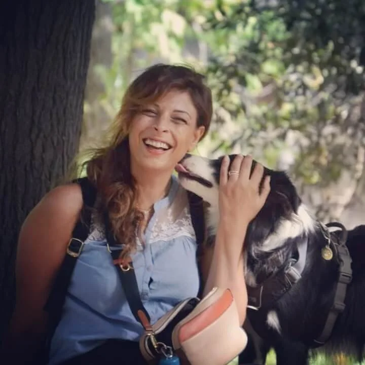 Leila, éducatrice canine Canifriendly, assise avec son chien qui lui fait une léchouille, illustrant une relation bienveillante et complicité sur la page d’accueil.