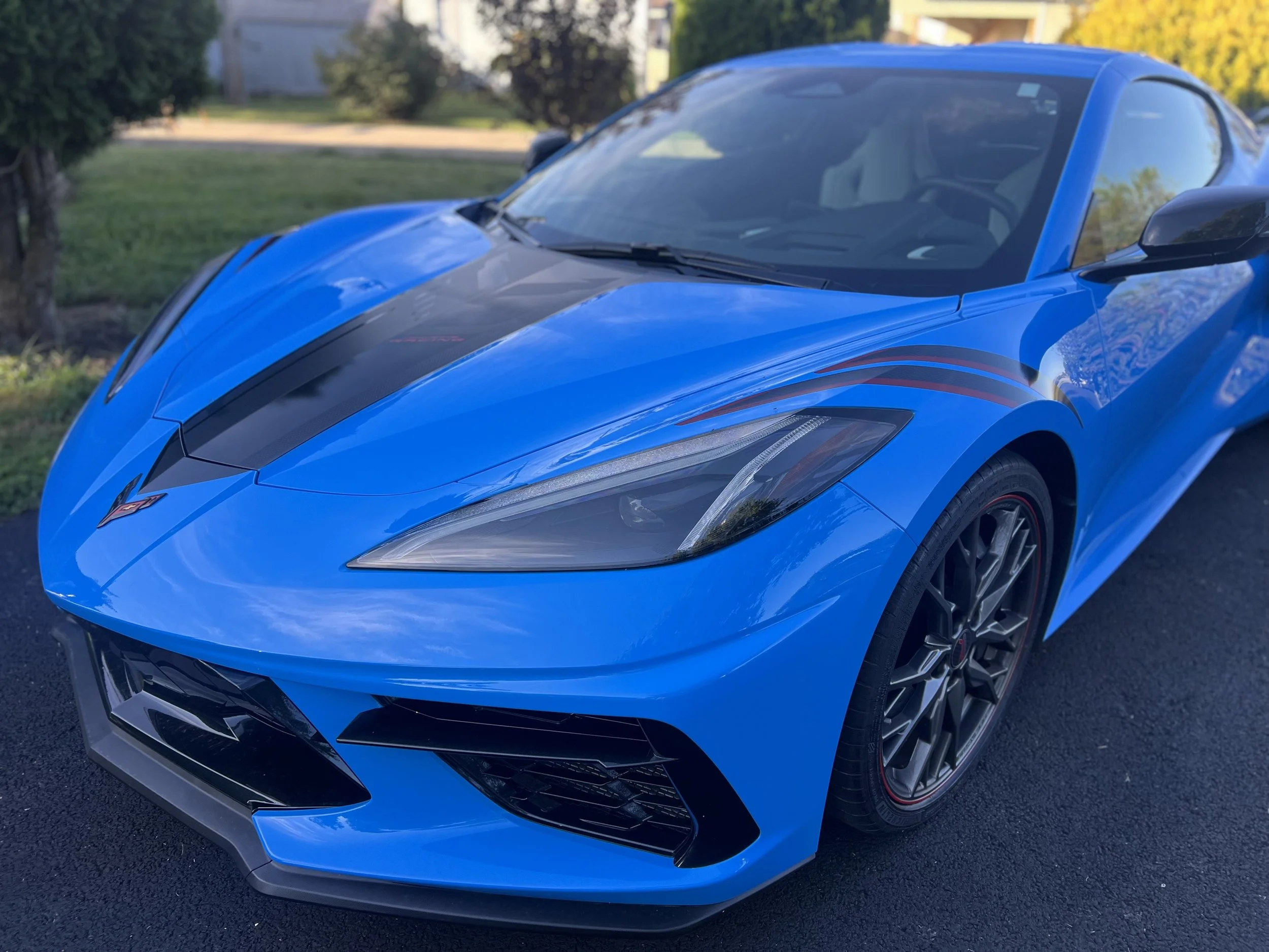 Blue sports car parked on a driveway with trees and lawn in the background.