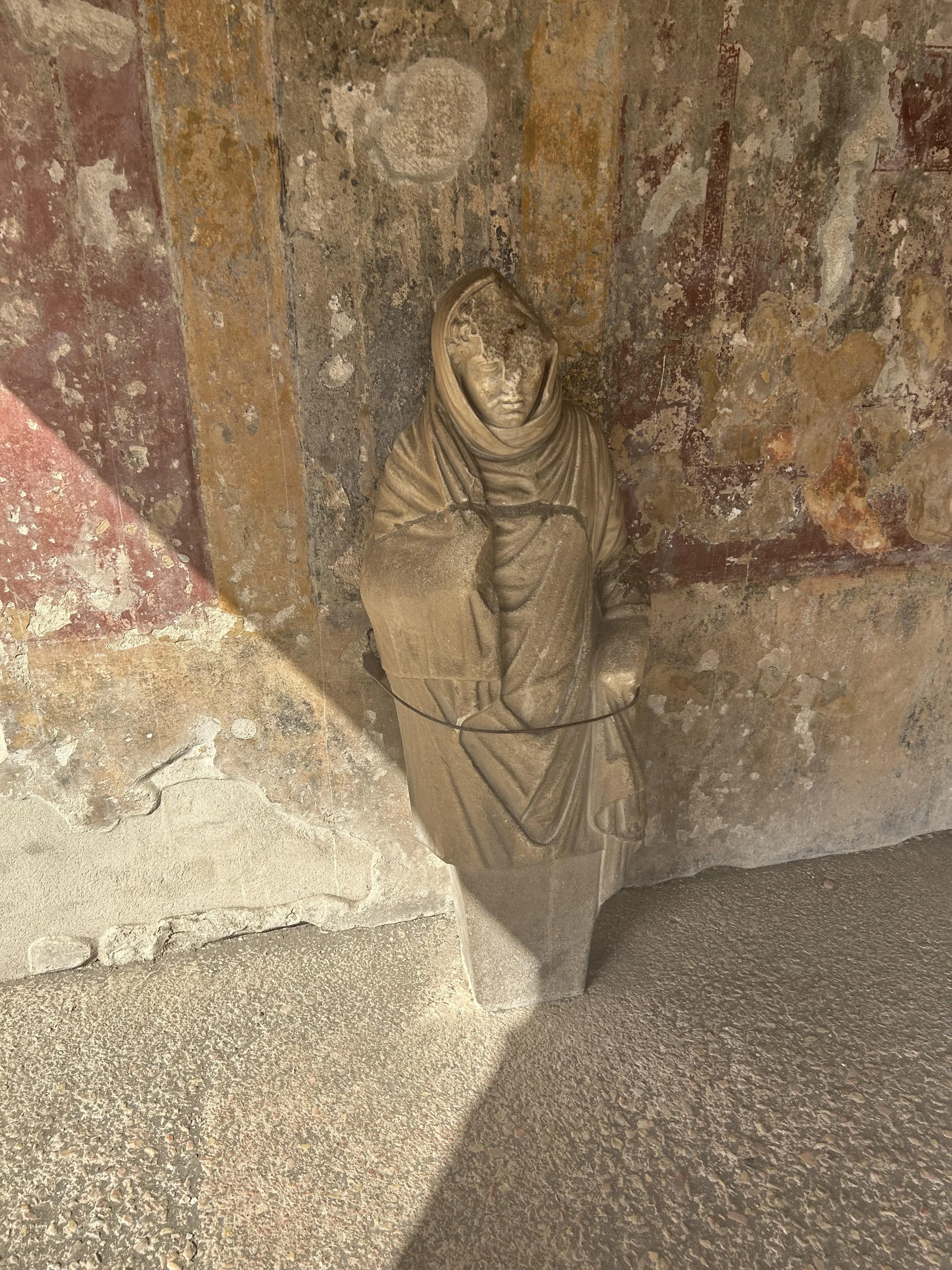 A statue of a woman in white stone. She has robes and her head is covered with a hood.