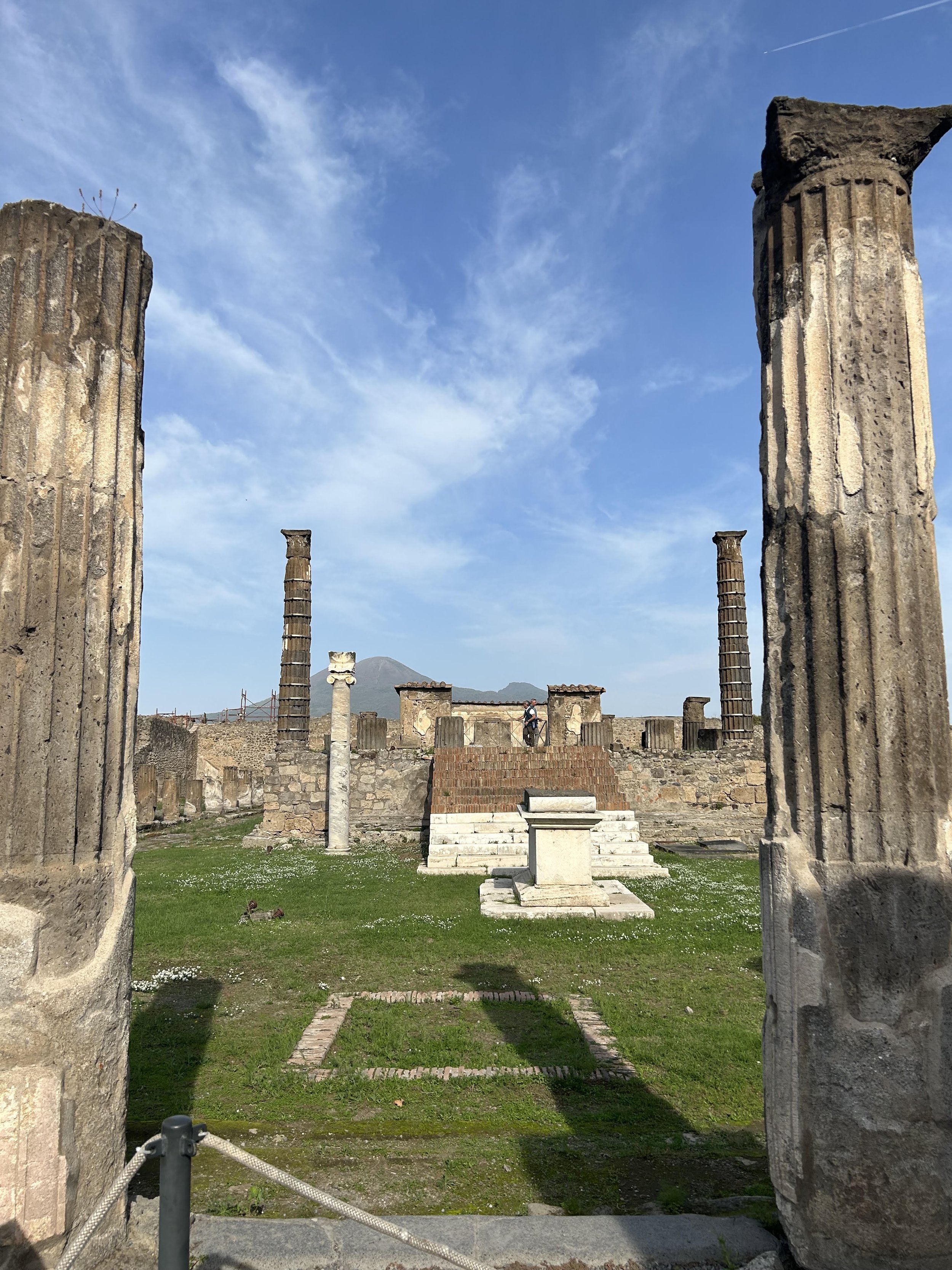 A large volcano looms in the distance between columns on top of a raised platform. An altar is in the centre in front of a series of steps.