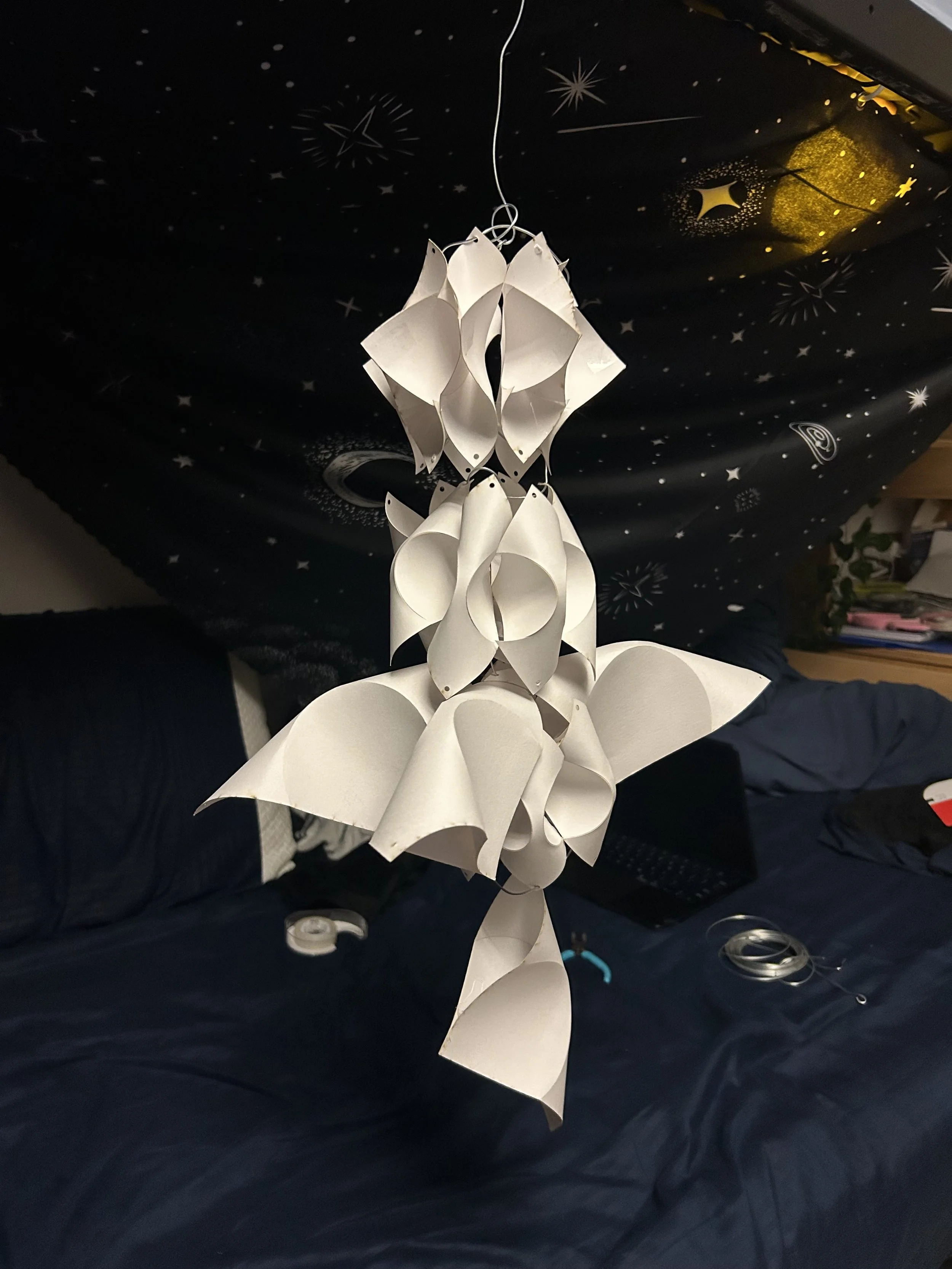 A large white paper star lantern hanging from the ceiling in a bedroom with space-themed wall decoration.