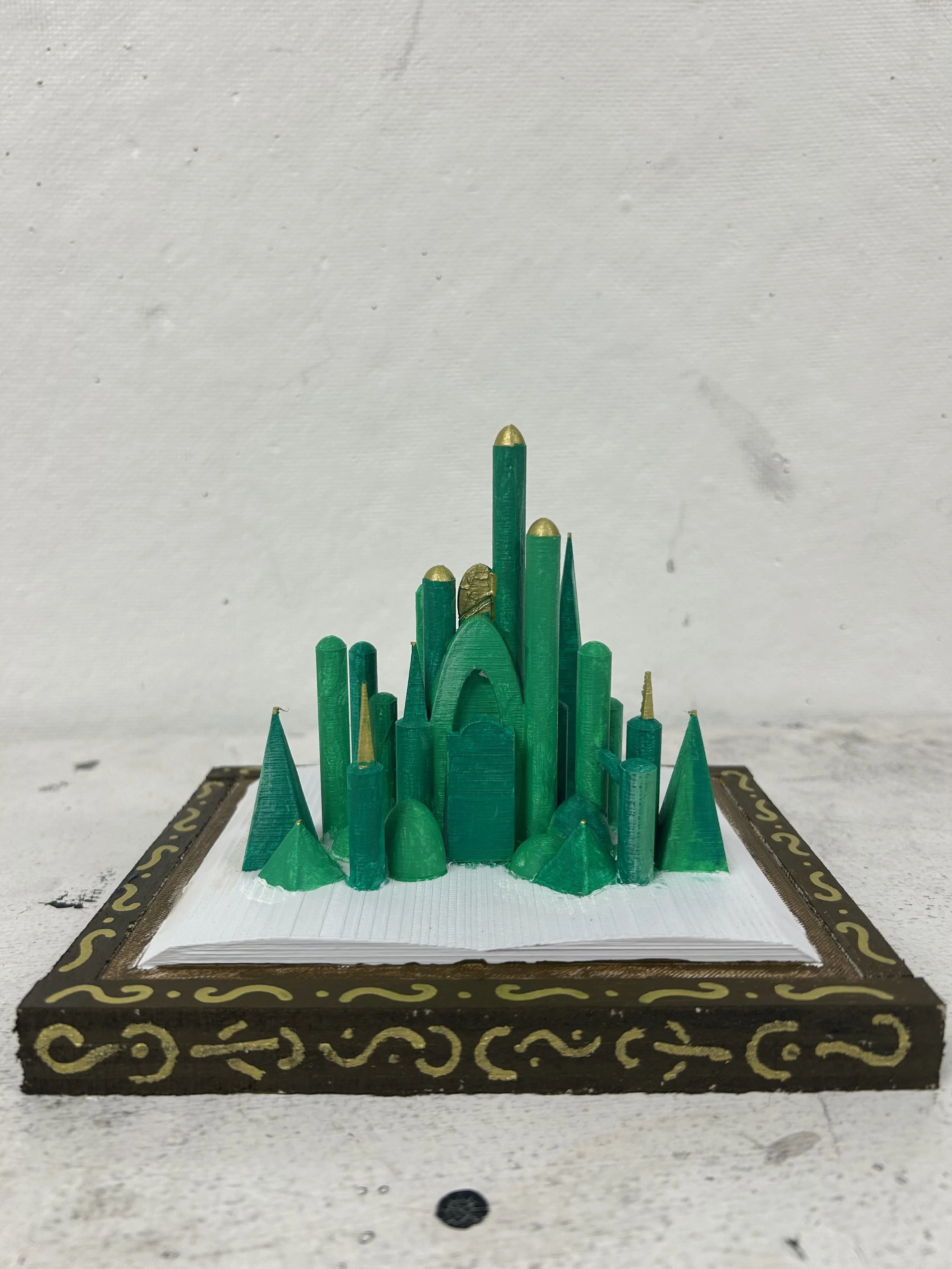 Model of a green castle with towers and spires, placed on a decorative frame.