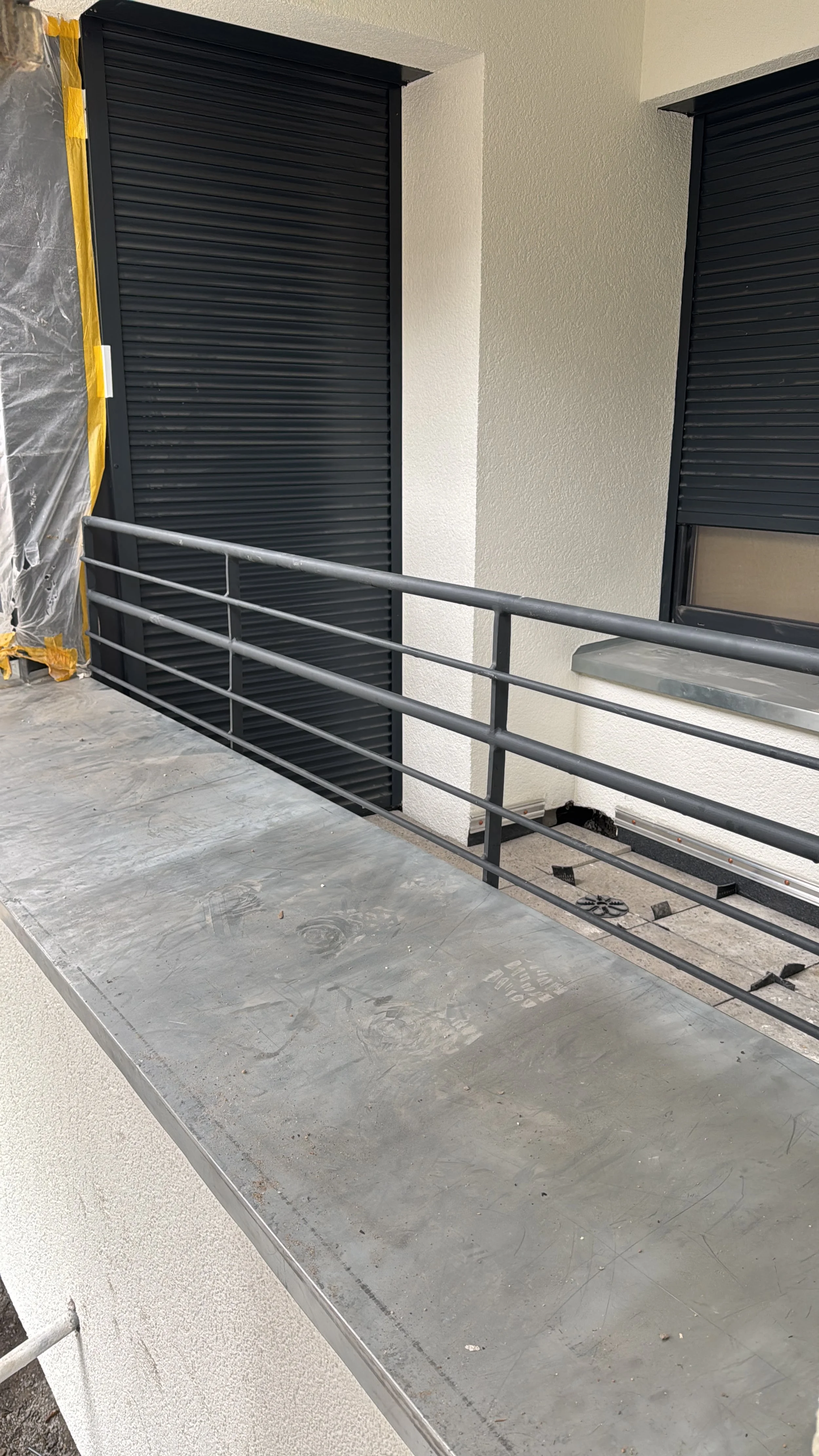 Balkon mit schwarzem Rollladen, Metallgeländer und ungefülltem Boden, Baustellenumgebung