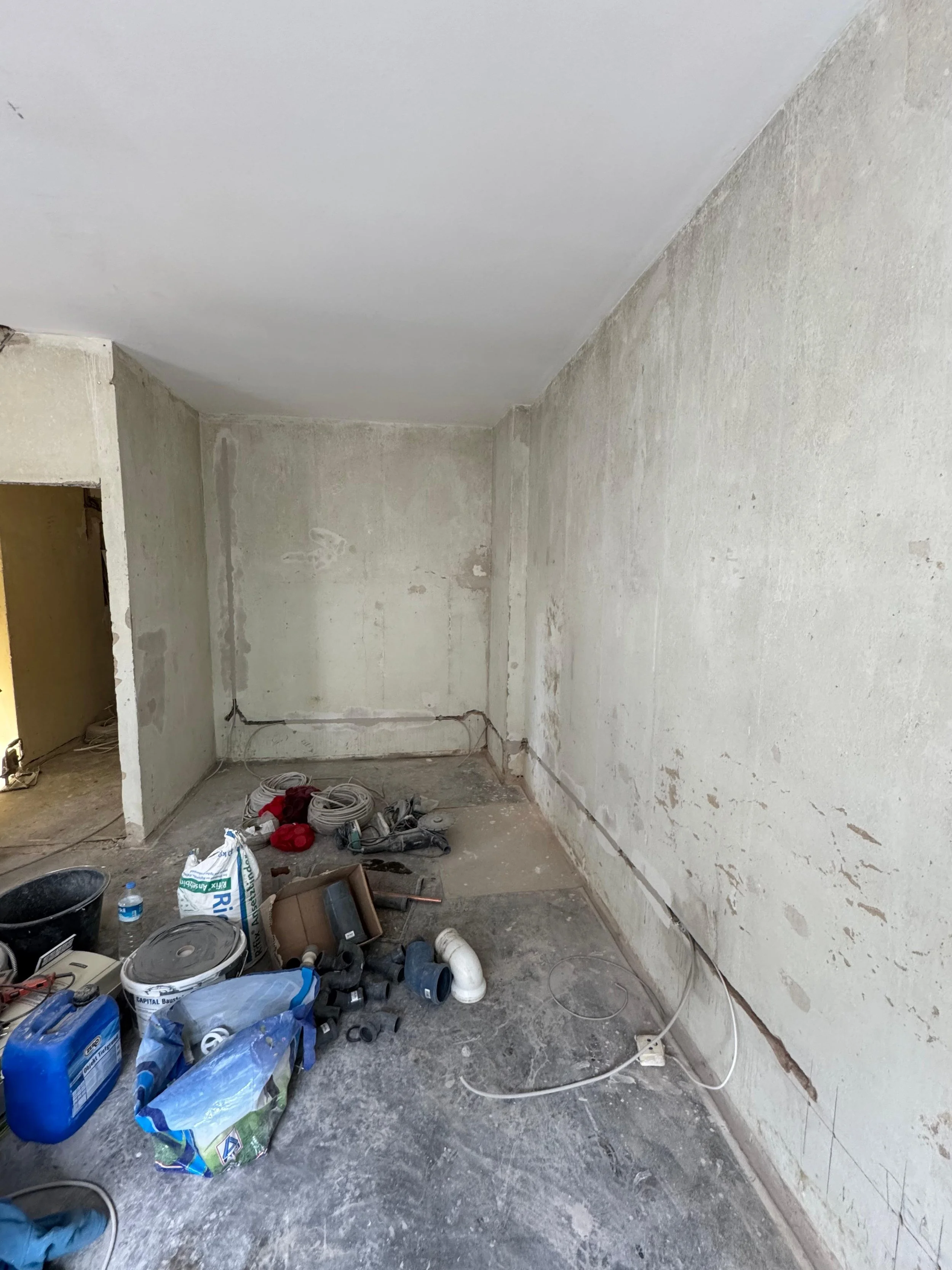 Innenraum eines Raumes im Bau oder Renovierung, mit Baustoffen, Werkzeugen und Rohren auf dem Boden, ungeputzte Wände und unvollständige Decke.