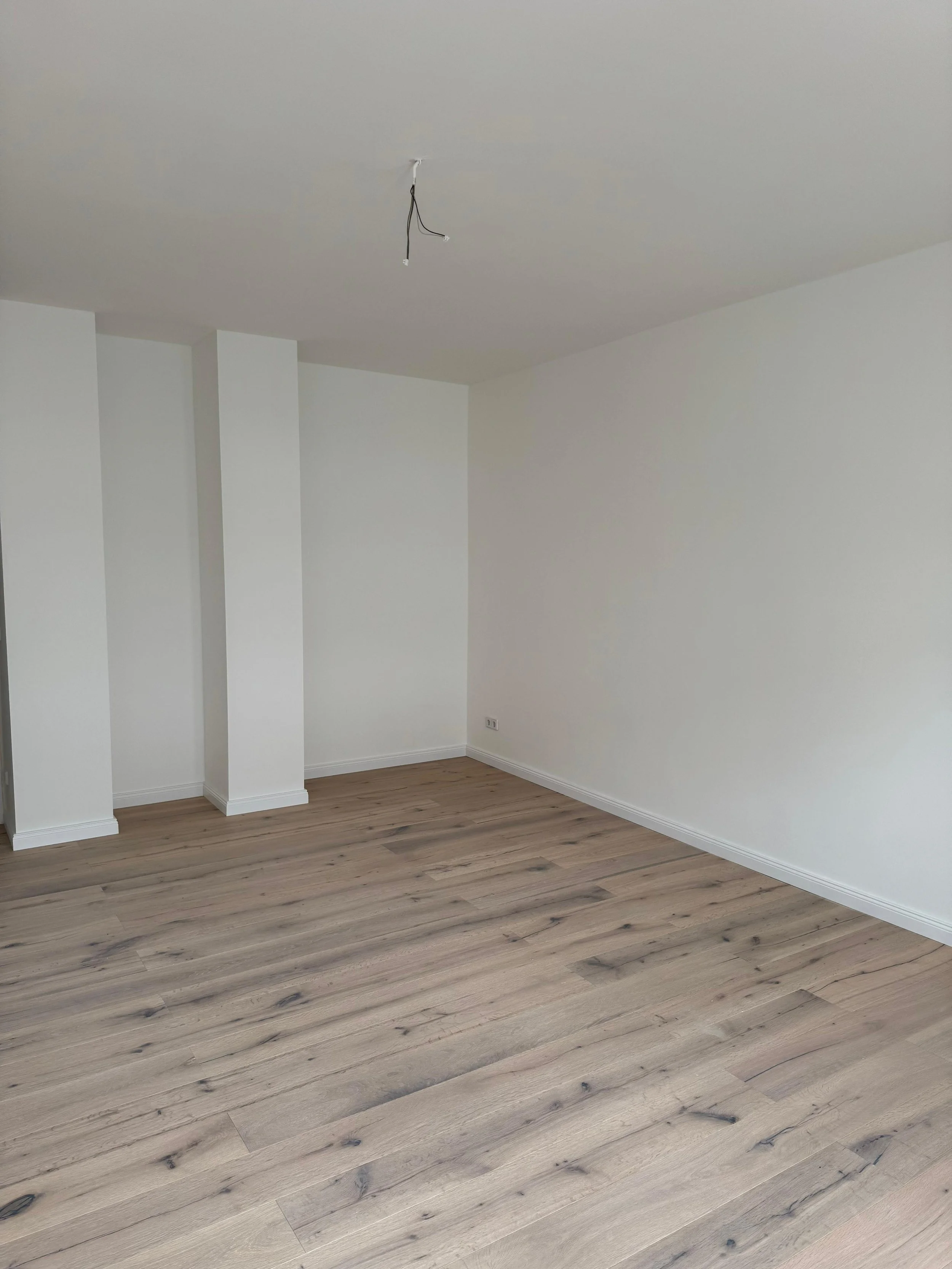 Leeres Zimmer mit weißen Wänden, Holzfußboden und einer Deckenlampe ohne Leuchtmittel