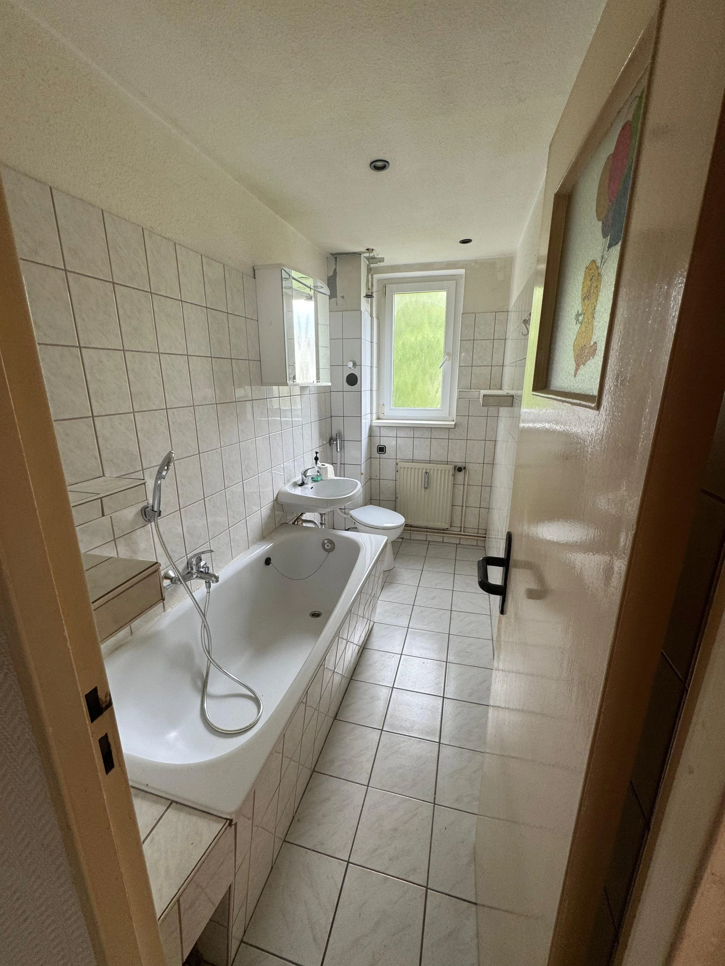 Ein Badezimmer mit Badewanne, Waschbecken, Toilette, Wandfliesen und Fenster.