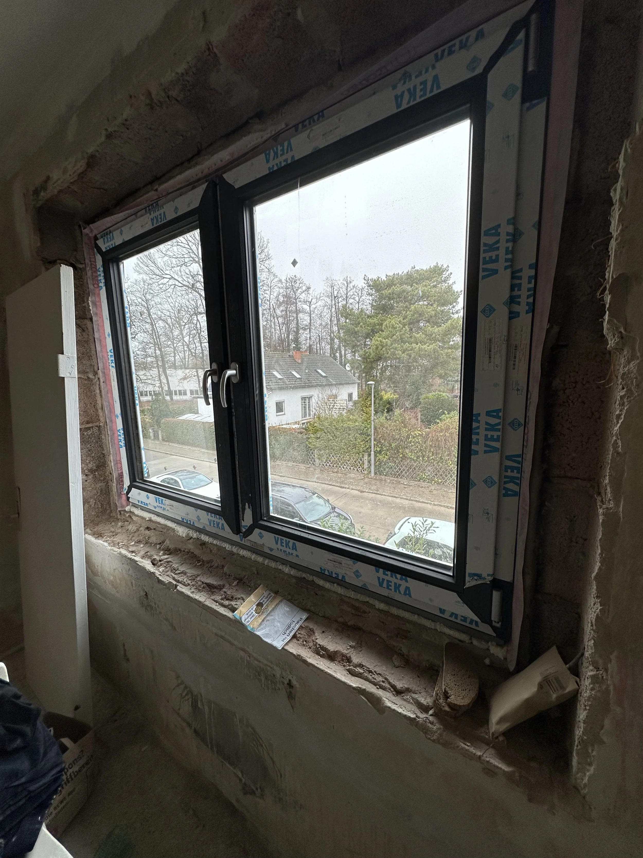 Ein neues PVC-Fenster in einem unfertigen Raum, mit Sicht auf eine Straße mit Autos und Häusern im Hintergrund.