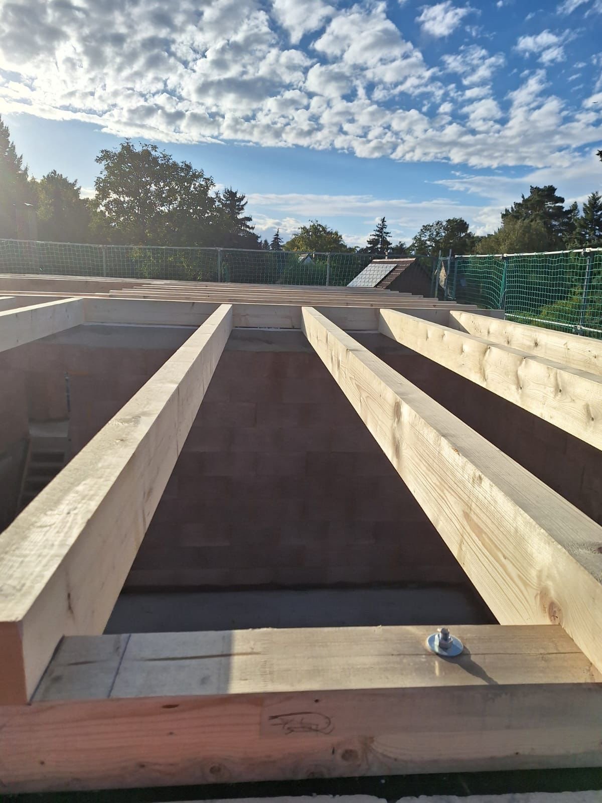 Bau eines Holzrahmens auf einer Baustelle im Freien, mit Himmel und Wolken im Hintergrund.