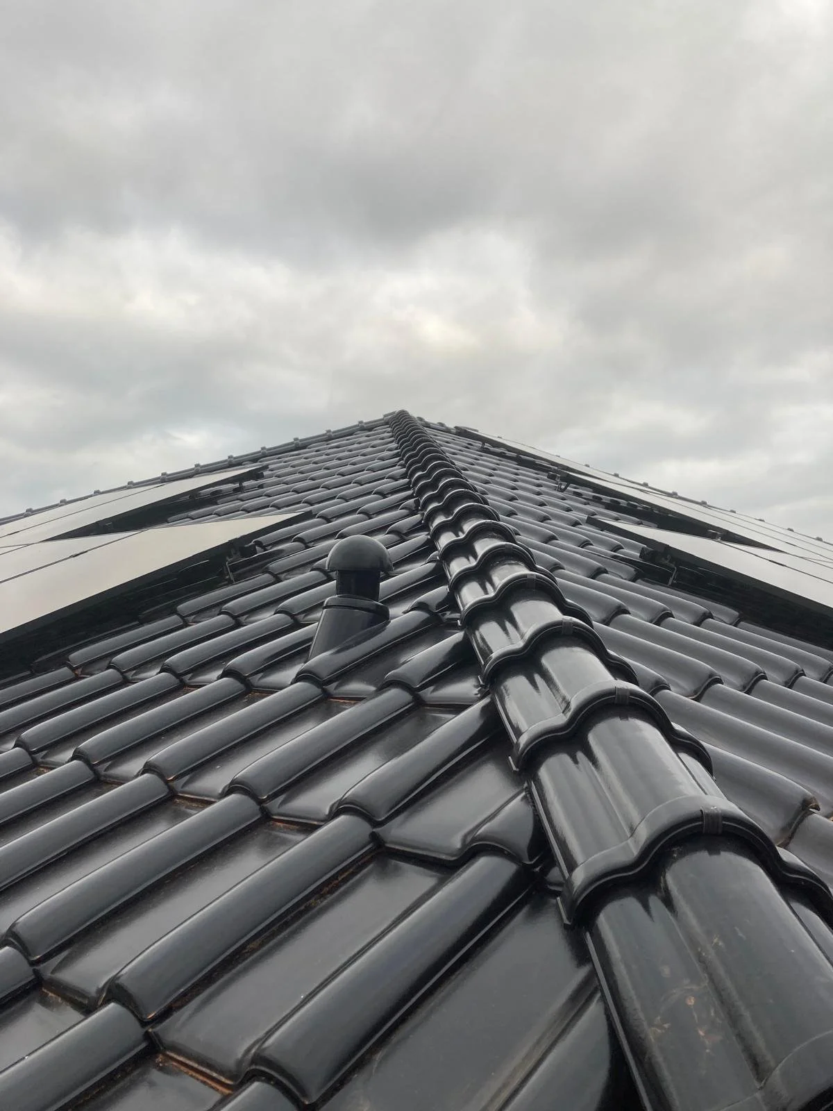Dach mit schwarzen Ziegeln und Regenrinnen, Blick nach oben, wolkiger Himmel