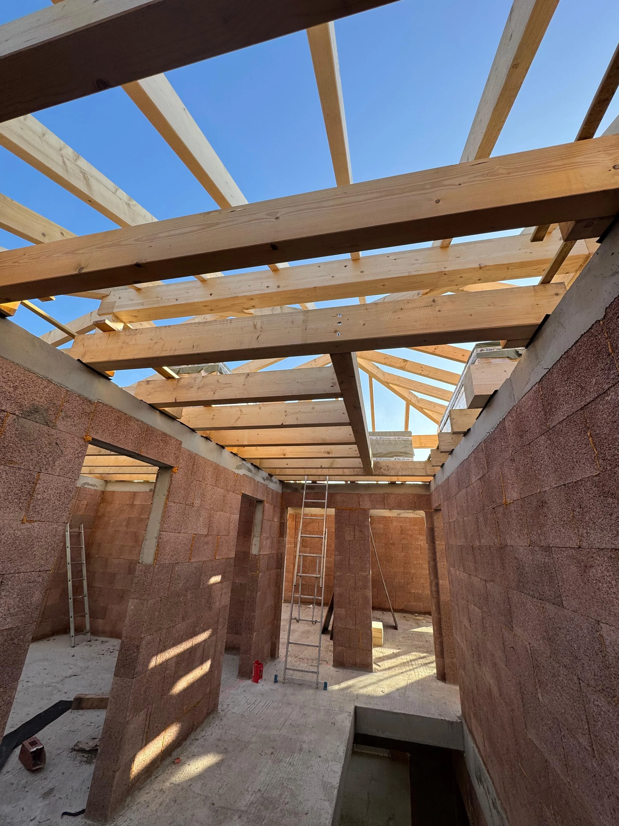 Bau eines Hauses mit sichtbaren Dachbalken, Ziegelwänden und einer Leiter im Inneren