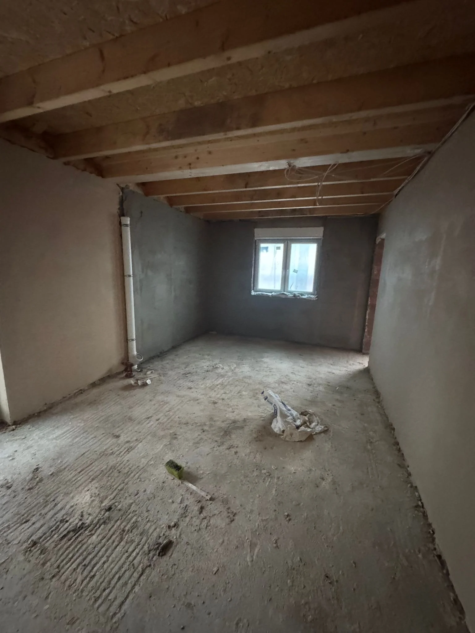 Ein Raum im Bauzustand mit unbehandeltem Boden, ungeputzten Wänden und sichtbaren Dachbalken.