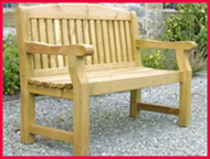 Wooden outdoor bench on a gravel surface with greenery in the background.