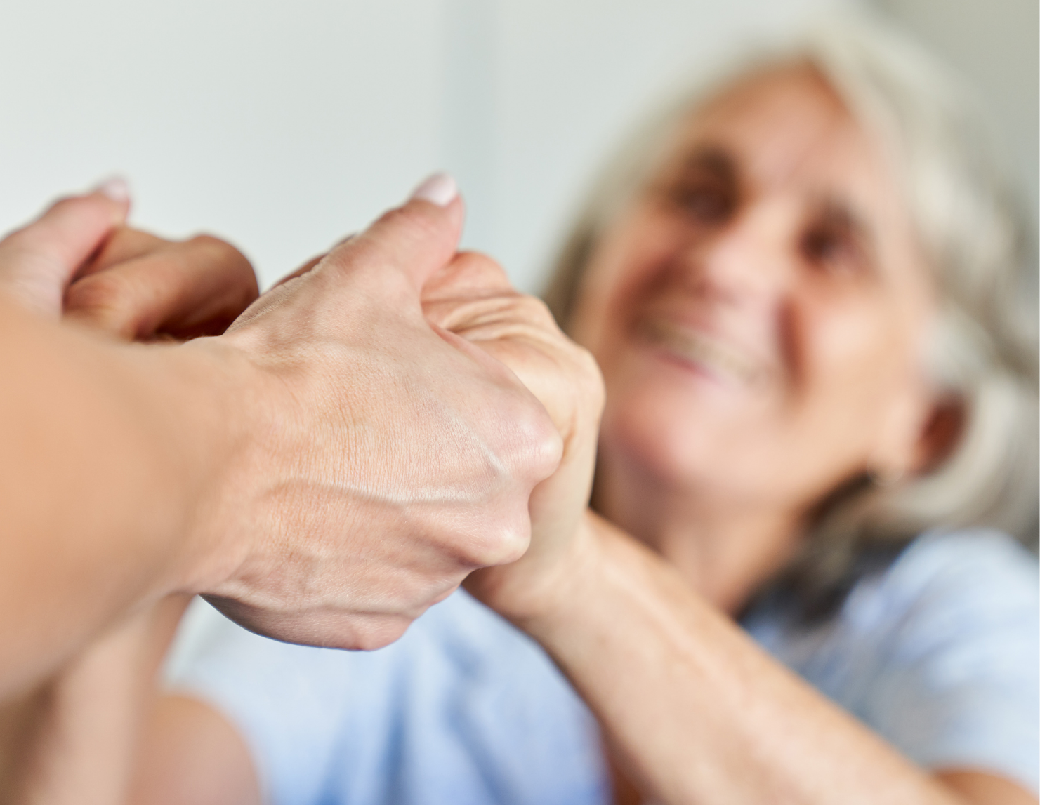 Two hands holding each other in the foreground with a smiling, older adult, in the background.