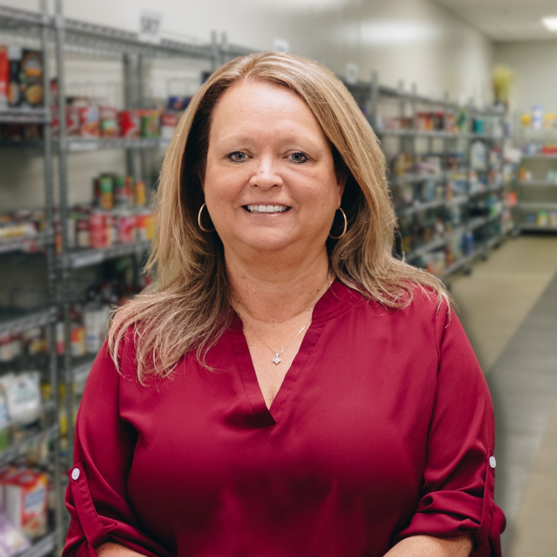 Roxanne is a white woman with longer, blonde hair. She is wearing a maroon blouse with shelves in the background.