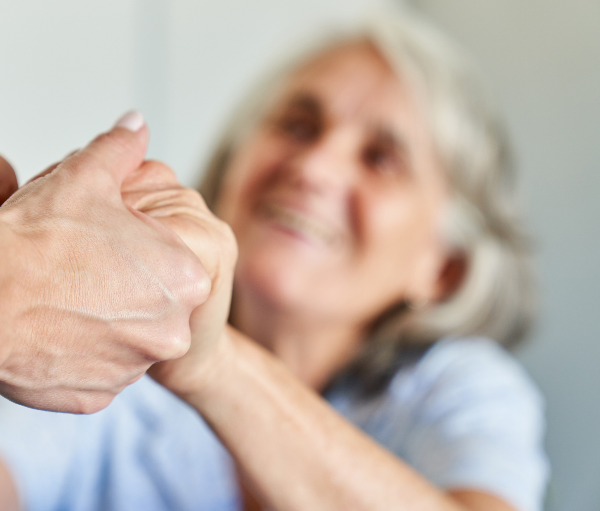 Two hands holding each other in the foreground with a smiling, older adult, in the background.