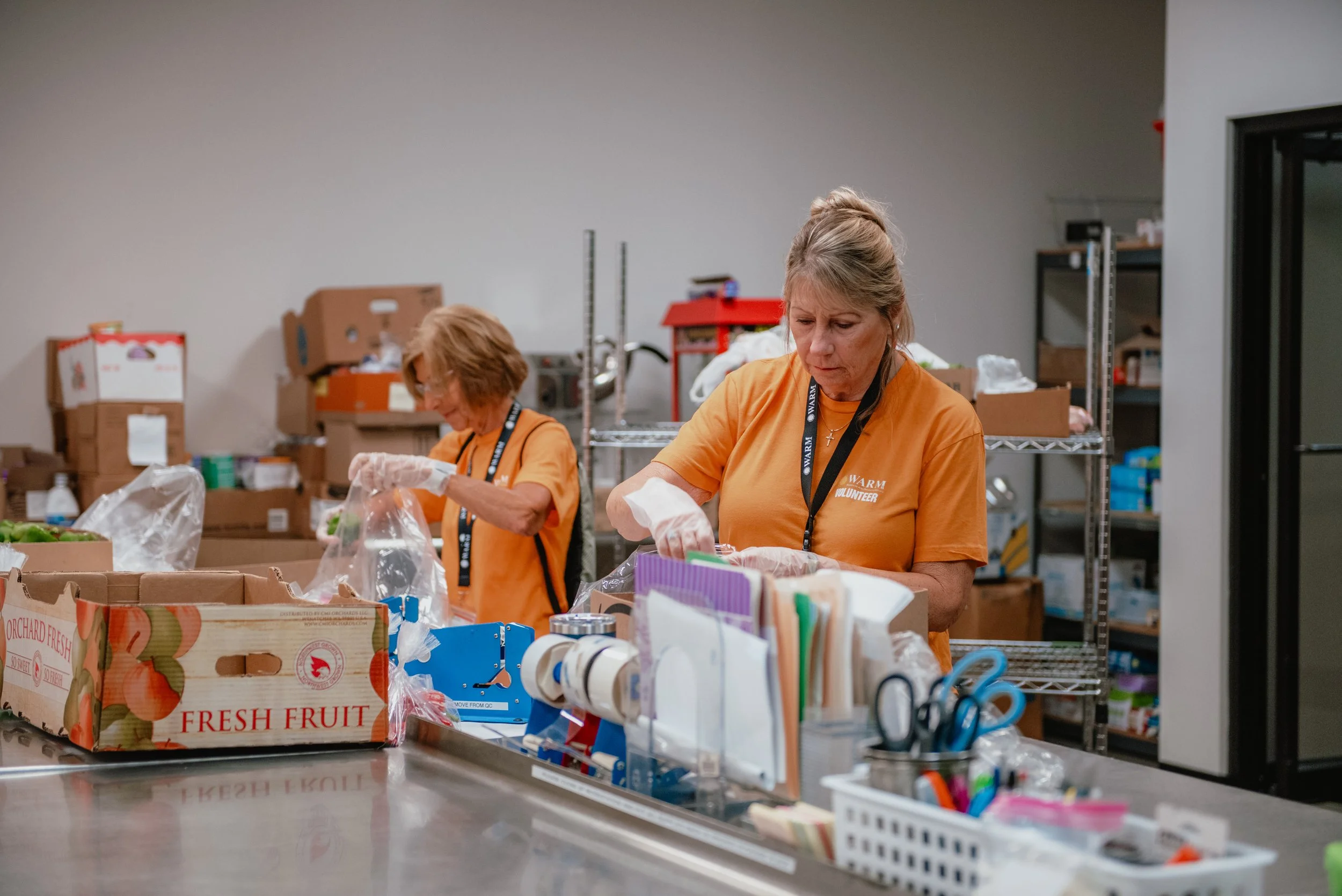 Two volunteers in orange shirts in quality control packing produce into separate bags for clients.