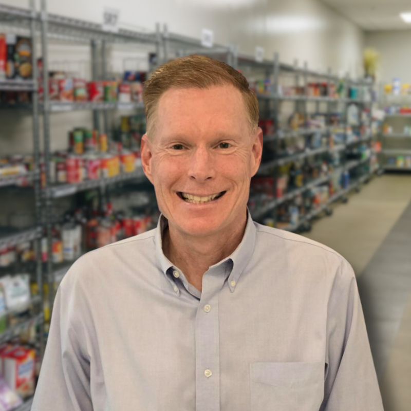 Matt is a white man with red hair. He is wearing a gray collared shirt with shelves in the background.