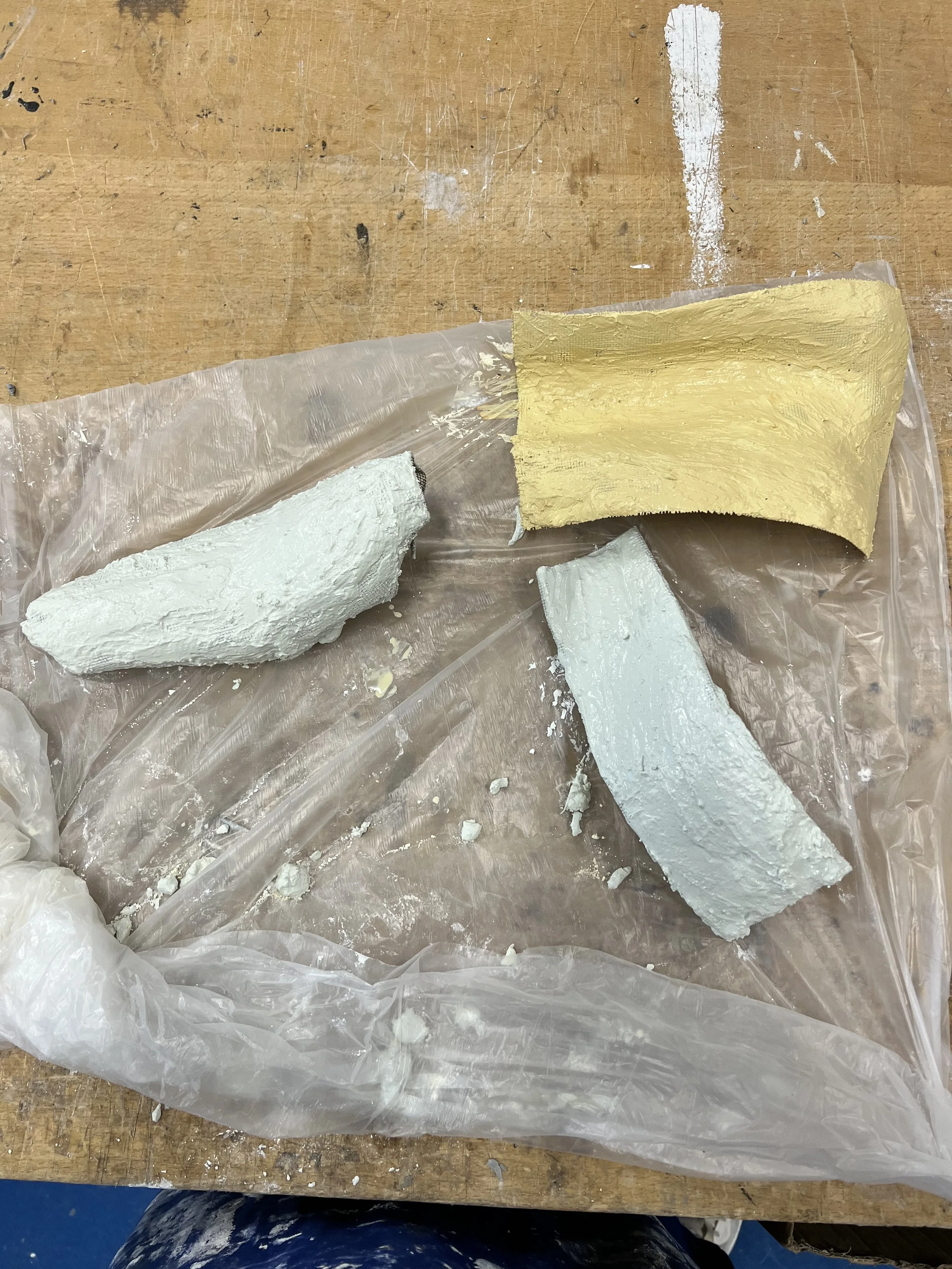 Three pieces of foam or plaster on a plastic sheet, on a wooden workbench.