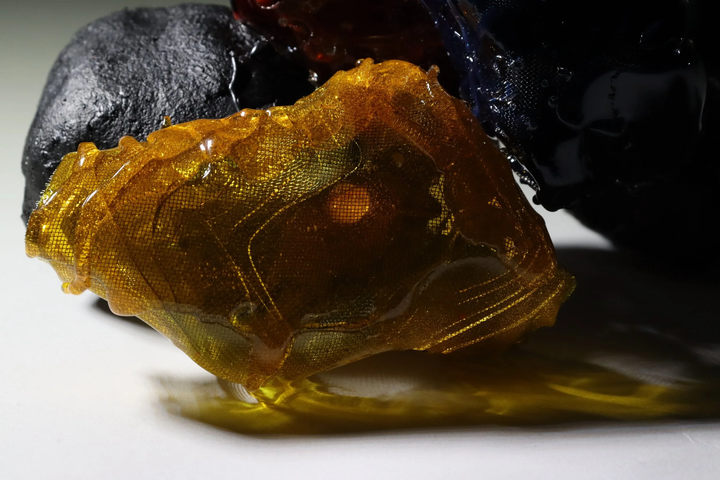 Close-up of two pieces of transcription resin, one black and one amber-colored, showing their detailed textures and glossy surfaces.