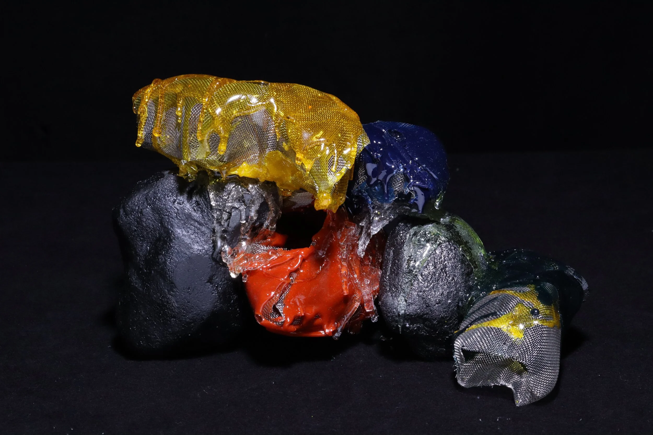 Colorful scraps of fabric and plastic melted and fused together on a black background.