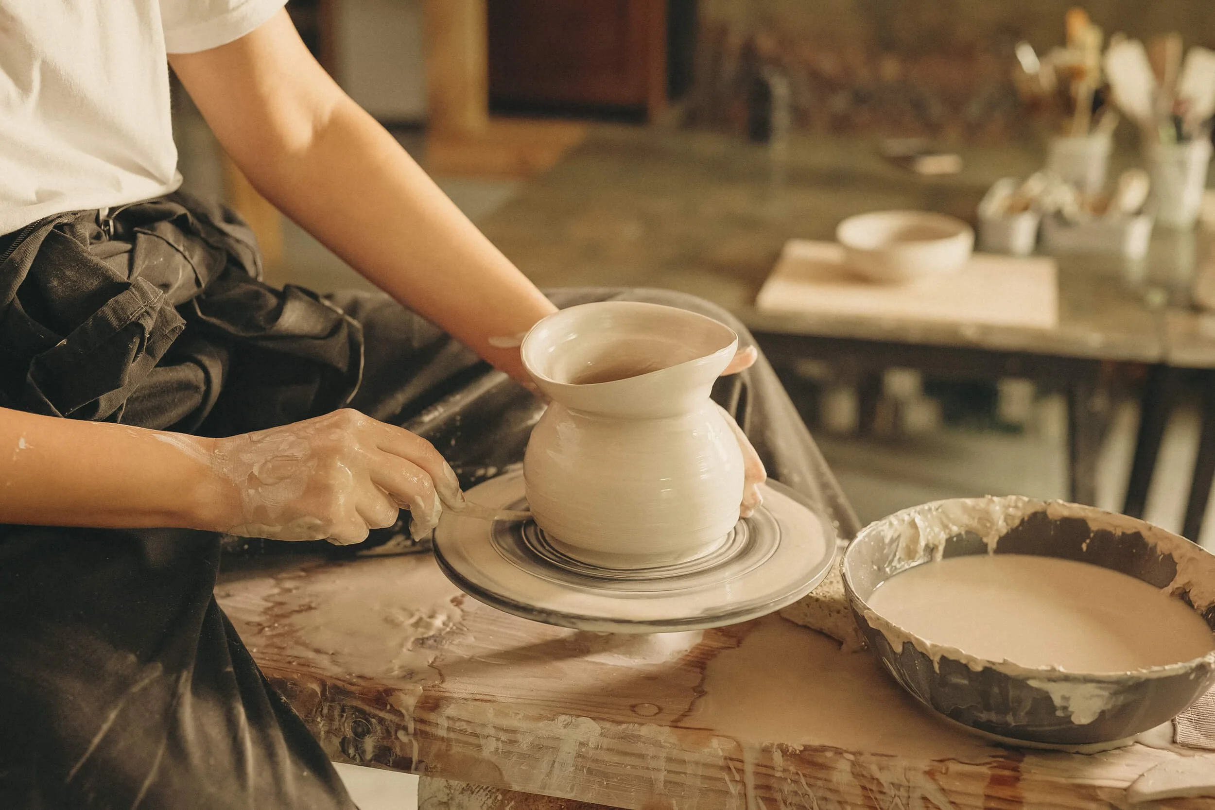 a woman at a potter's wheel shaping a vase