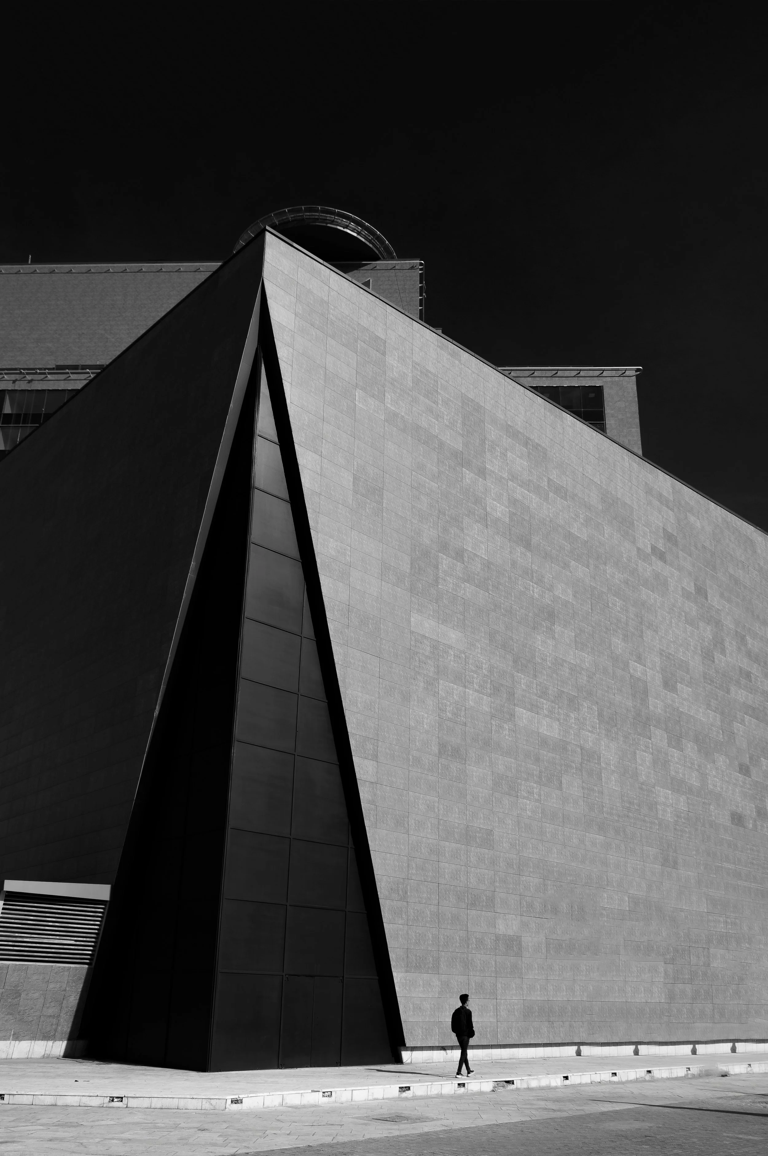 Black and white photo of modern architectural building with geometric facade and a person walking nearby.