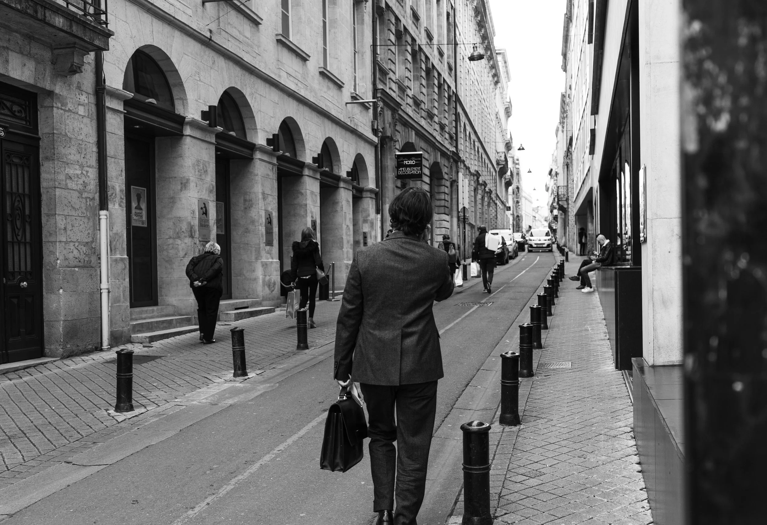 A man in a suit carrying a briefcase walking down a city sidewalk with several pedestrians along the street.