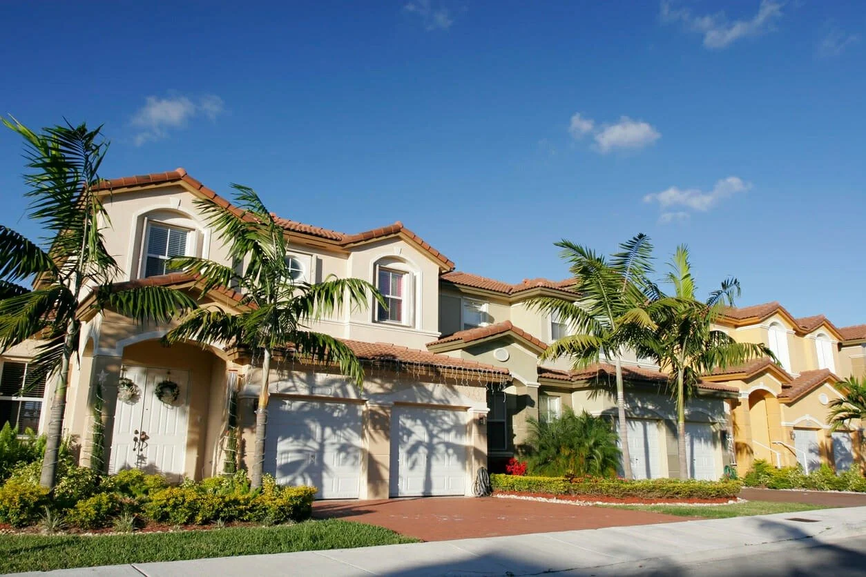 Row of modern townhouses with white garage doors, palm trees, and a clear blue sky in Florida.
