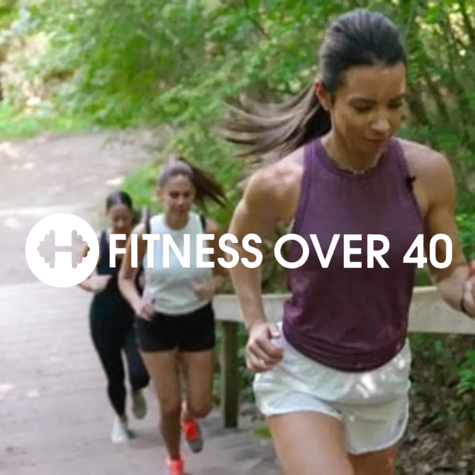 Three women jogging on a forest trail with green trees in the background, one woman in front wearing a purple tank top and white shorts, two women behind them wearing athletic outfits.