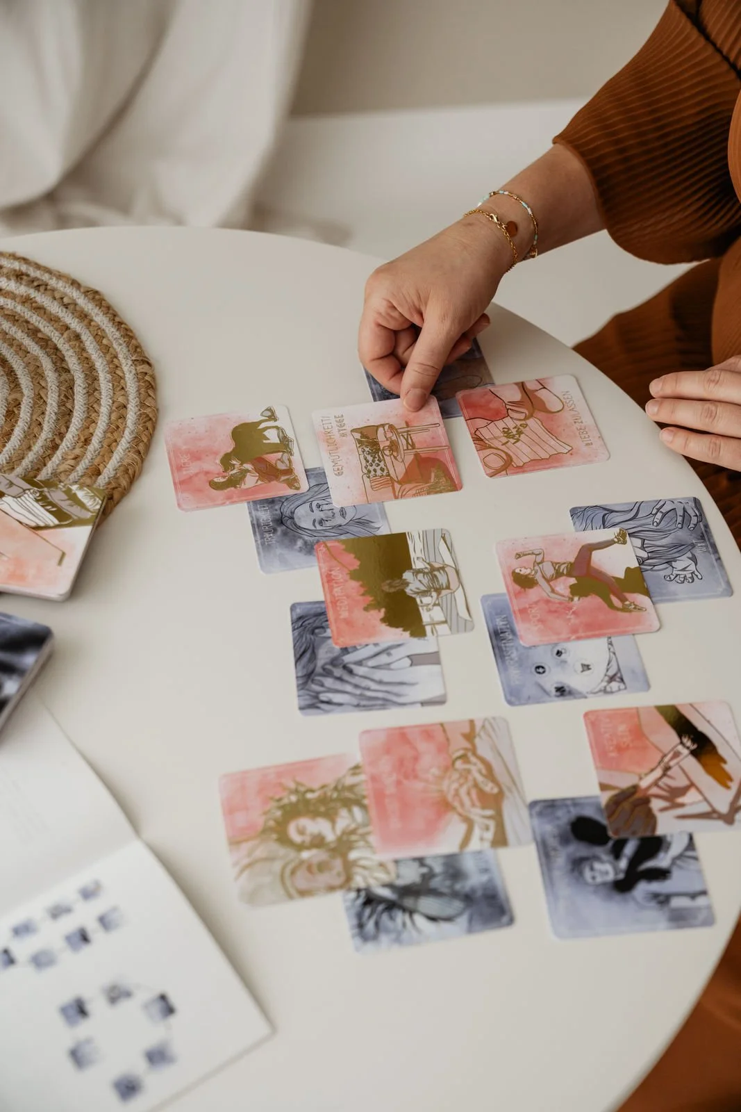 Person legt Karten auf einem Tisch, die Illustrationen von Frauen in verschiedenen Szenen zeigen.