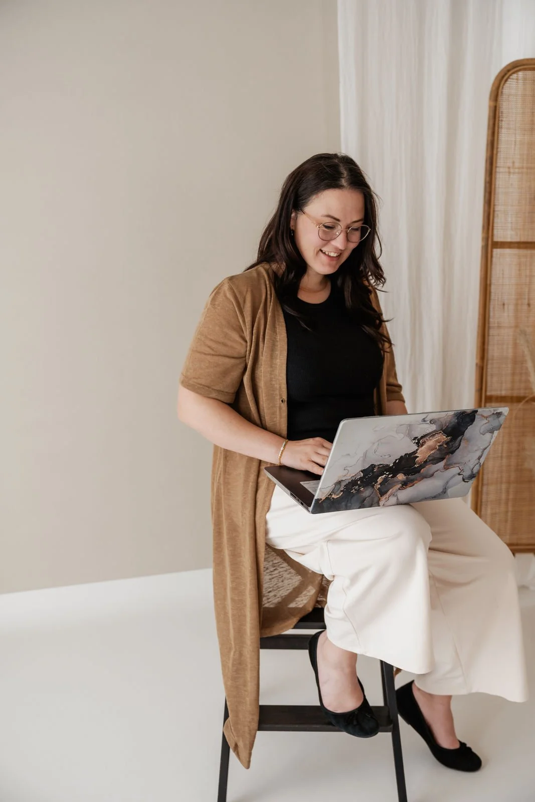 Eine Frau sitzt auf einem Stuhl, hat einen Laptop auf den Knien und lächelt, während sie arbeitet.