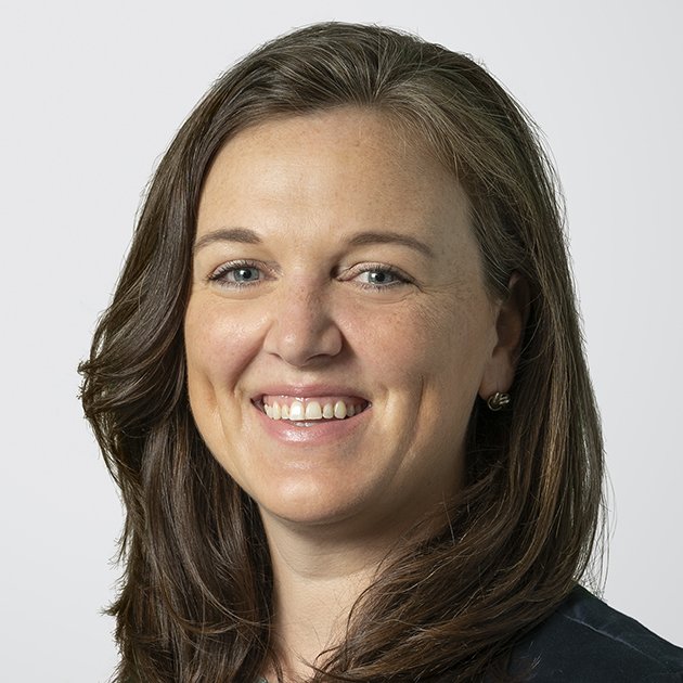 Close-up of a woman with shoulder-length brown hair, blue eyes, and wearing a dark top, smiling at the camera.