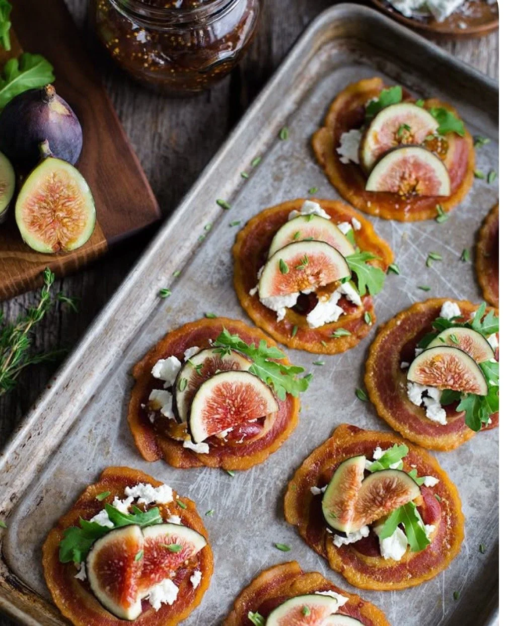Appetizers with sliced figs, crumbled cheese, and greens on a baking sheet.