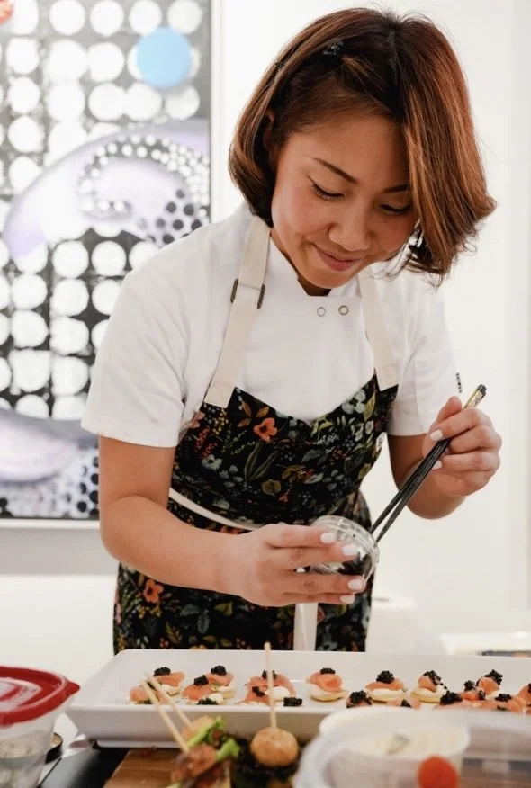 Woman decorating appetizers on a platter in a kitchen.