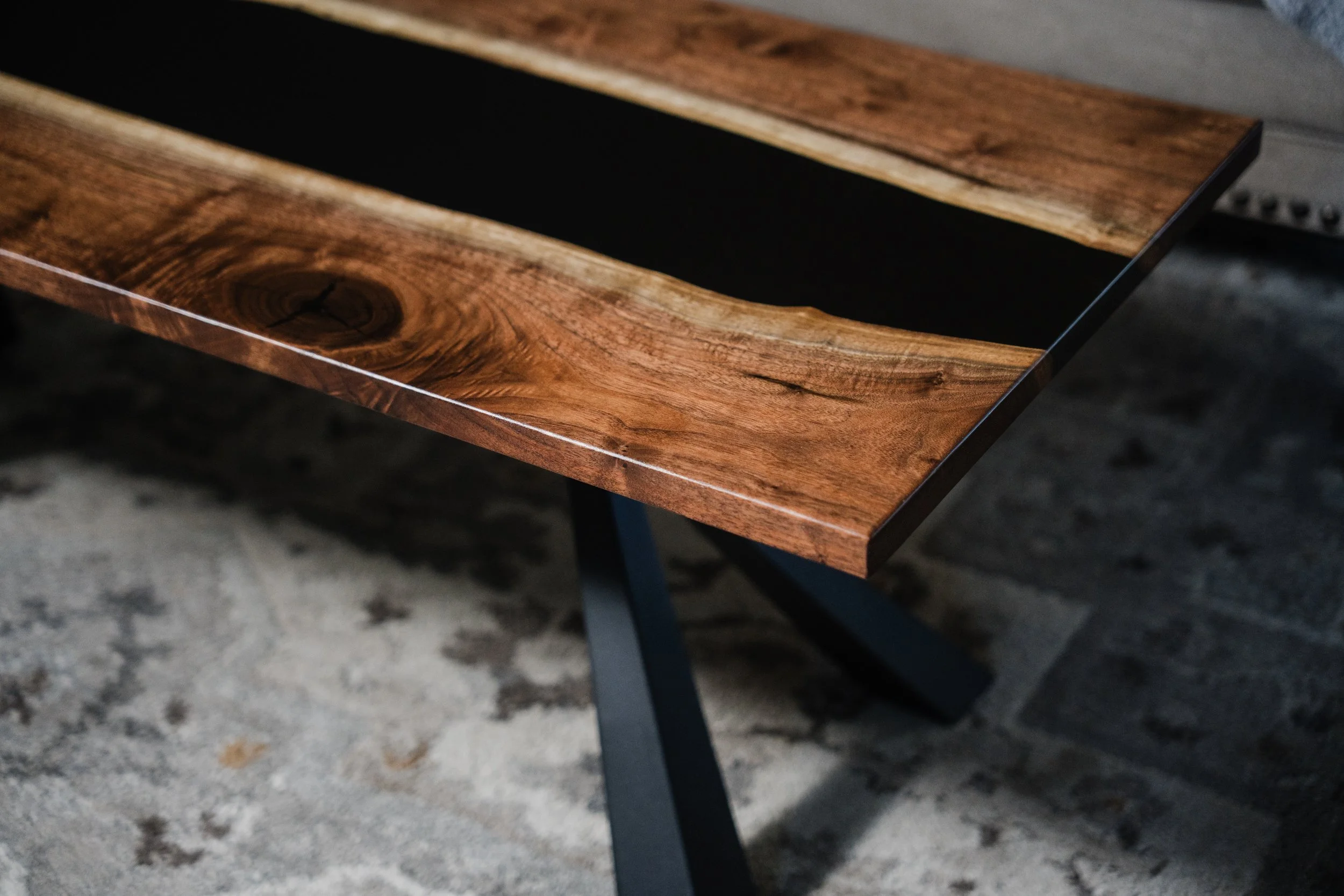 Close-up of a wooden table with a glossy finish, showing natural wood grain and knots, with black metal legs.